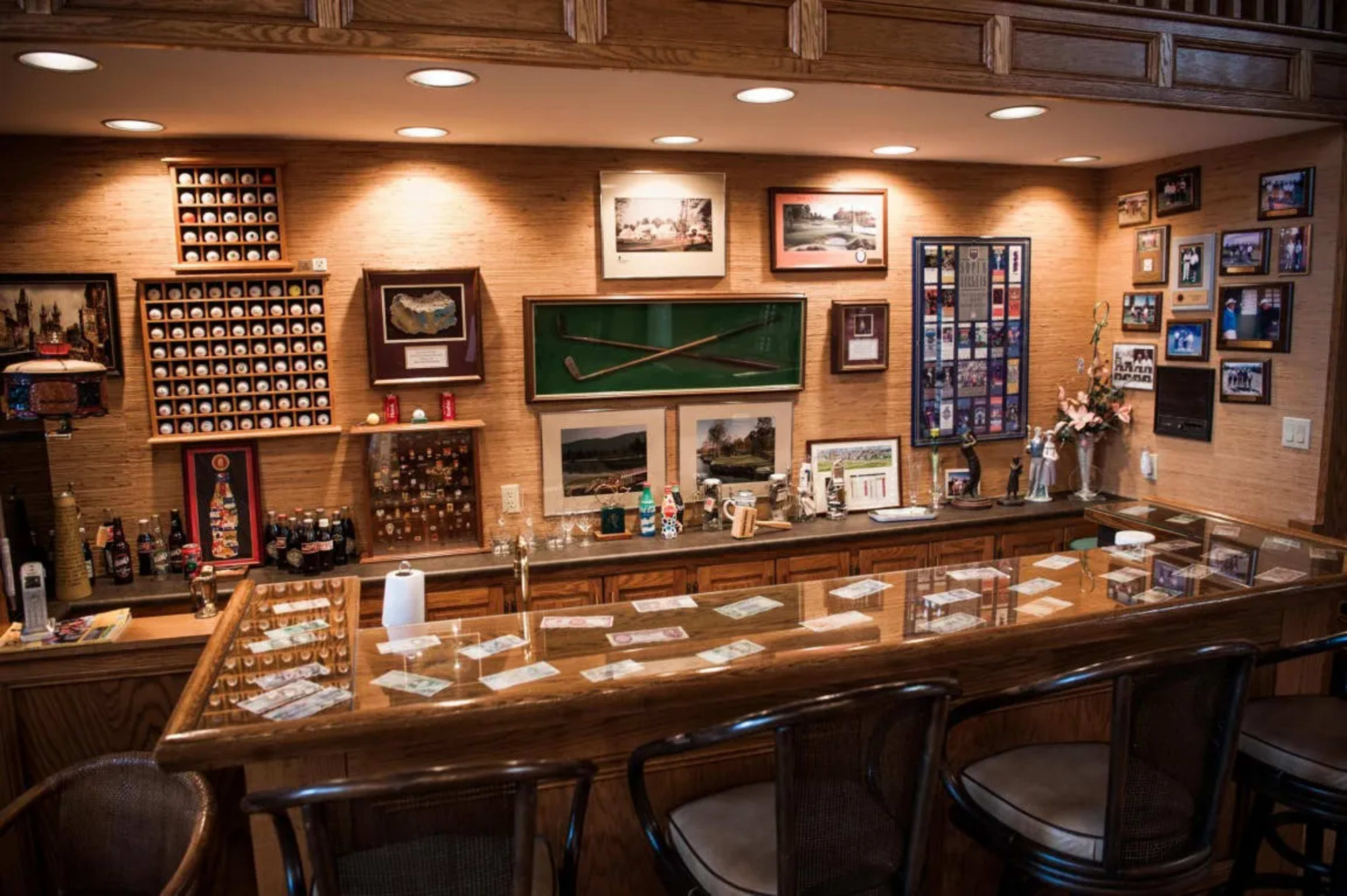 A wooden bar area with a polished countertop, shelves displaying golf memorabilia, and framed photographs on the walls.