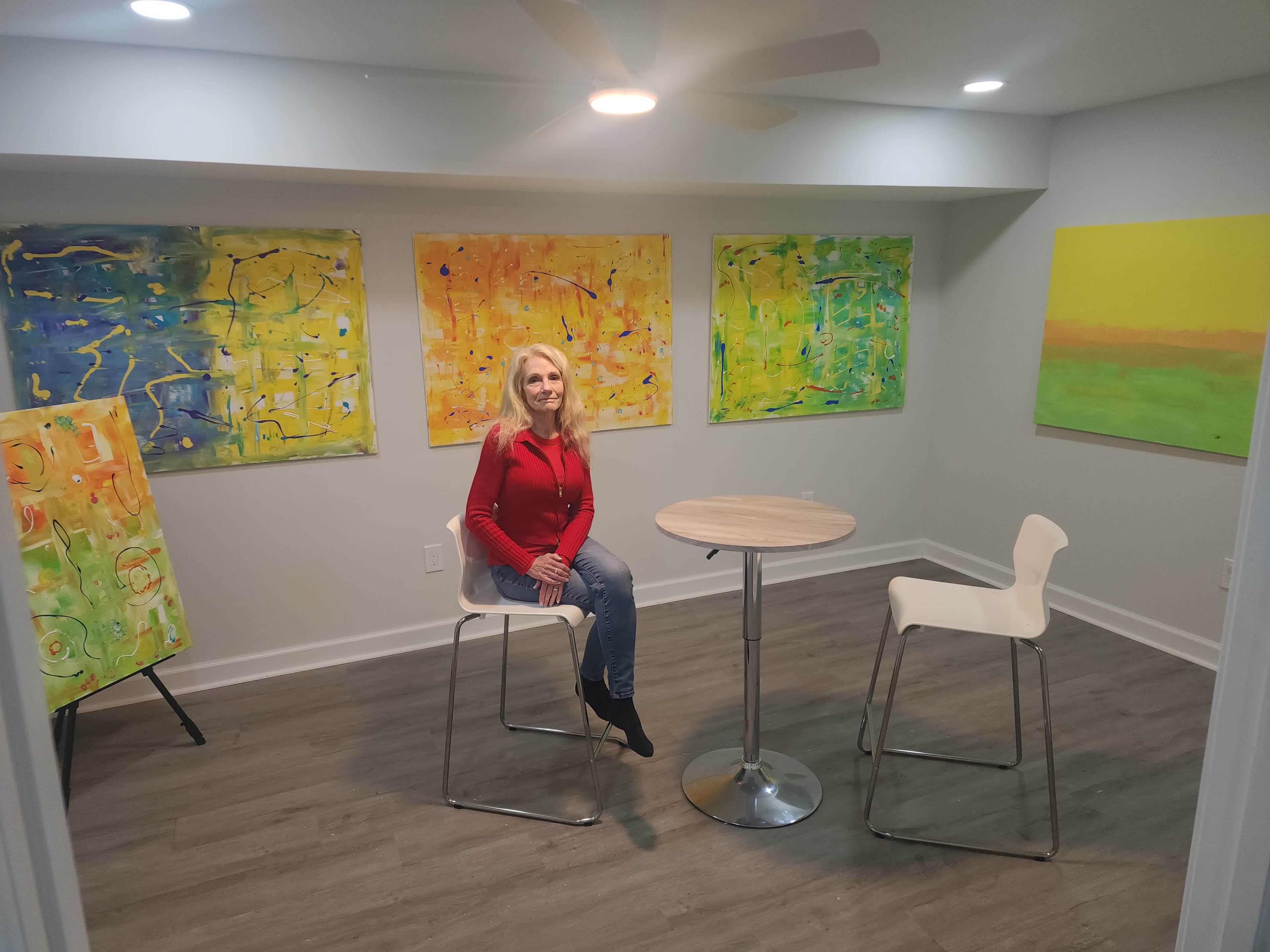 A woman sits at a round table in a room adorned with vibrant abstract paintings on the walls.