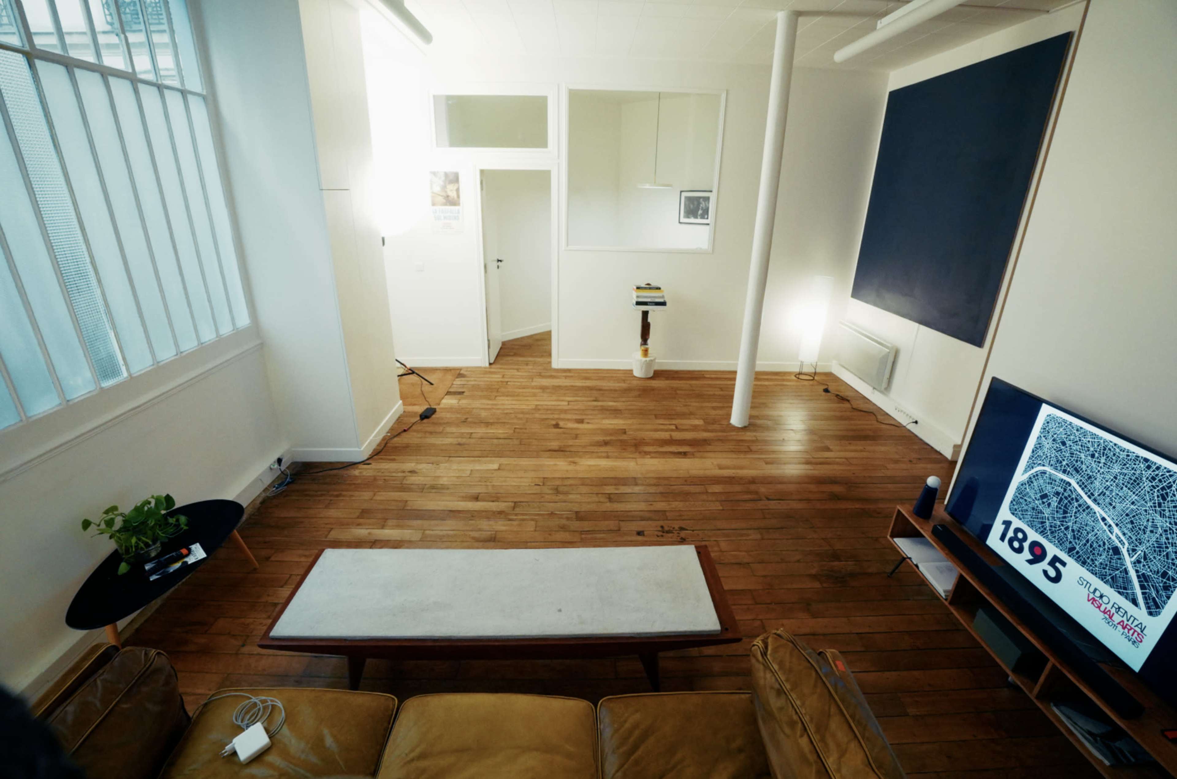 The image shows a spacious, minimalist living room with wooden flooring, a coffee table, a large television, and a light source illuminating the area.