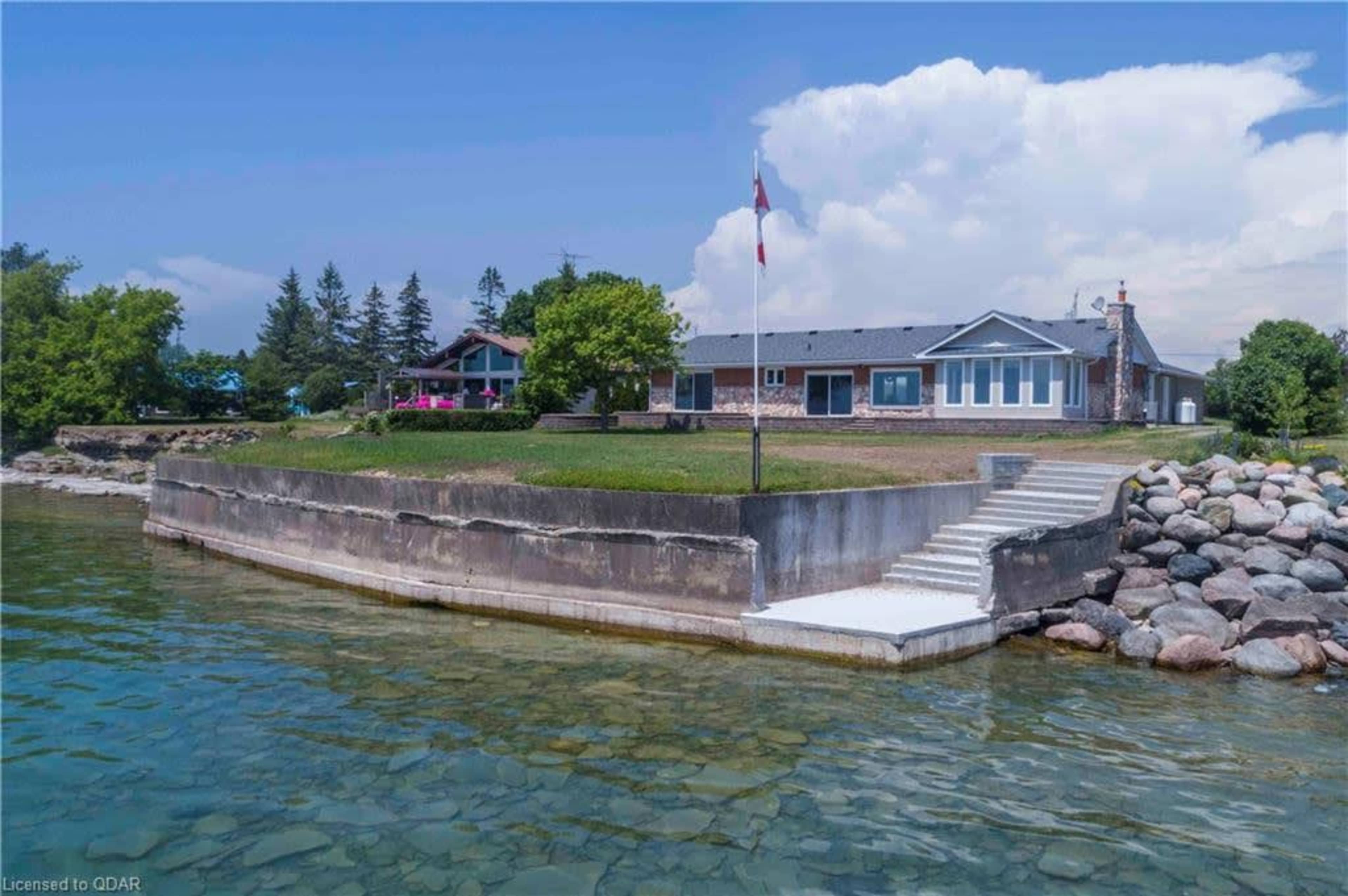 A lakeside property features a stone wall shoreline, a grassy area, and a building with multiple windows.