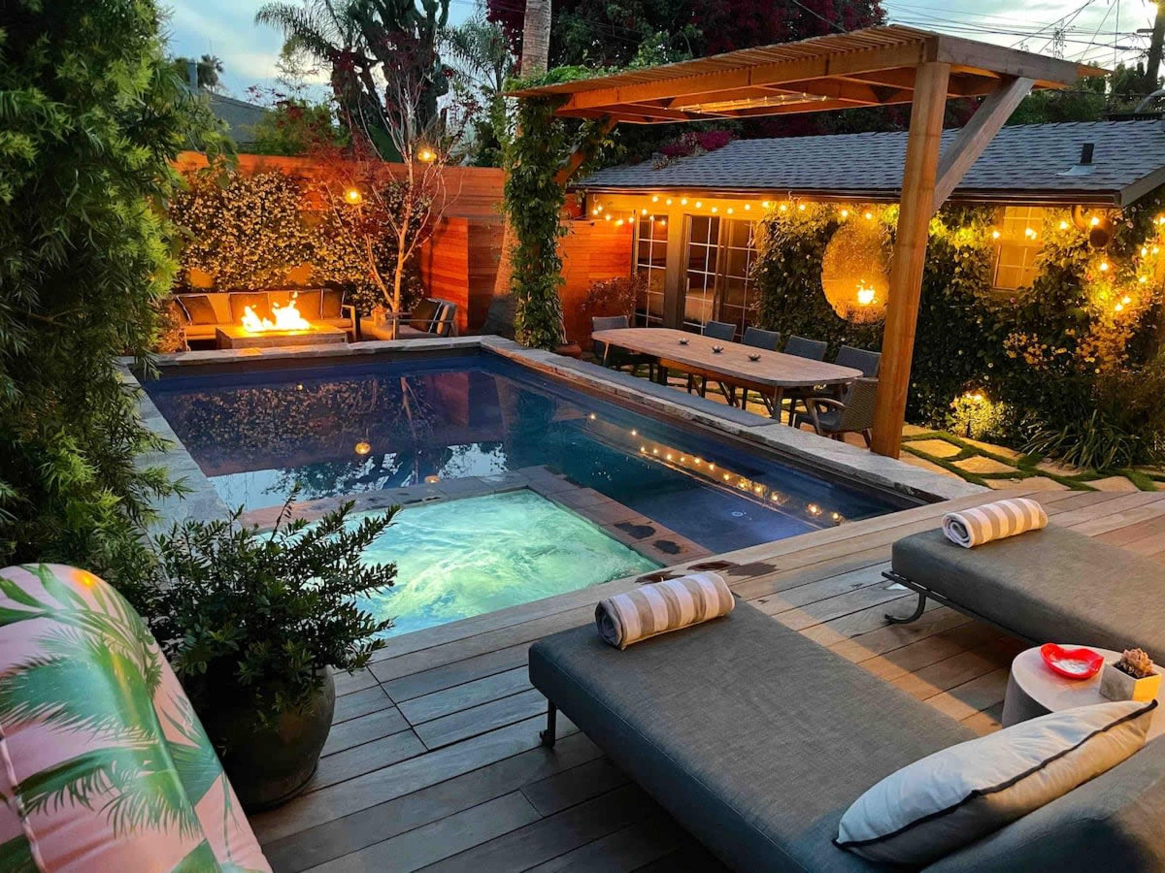 The scene features a backyard with a swimming pool, a hot tub, and lounge chairs, all illuminated by string lights in a landscaped setting.