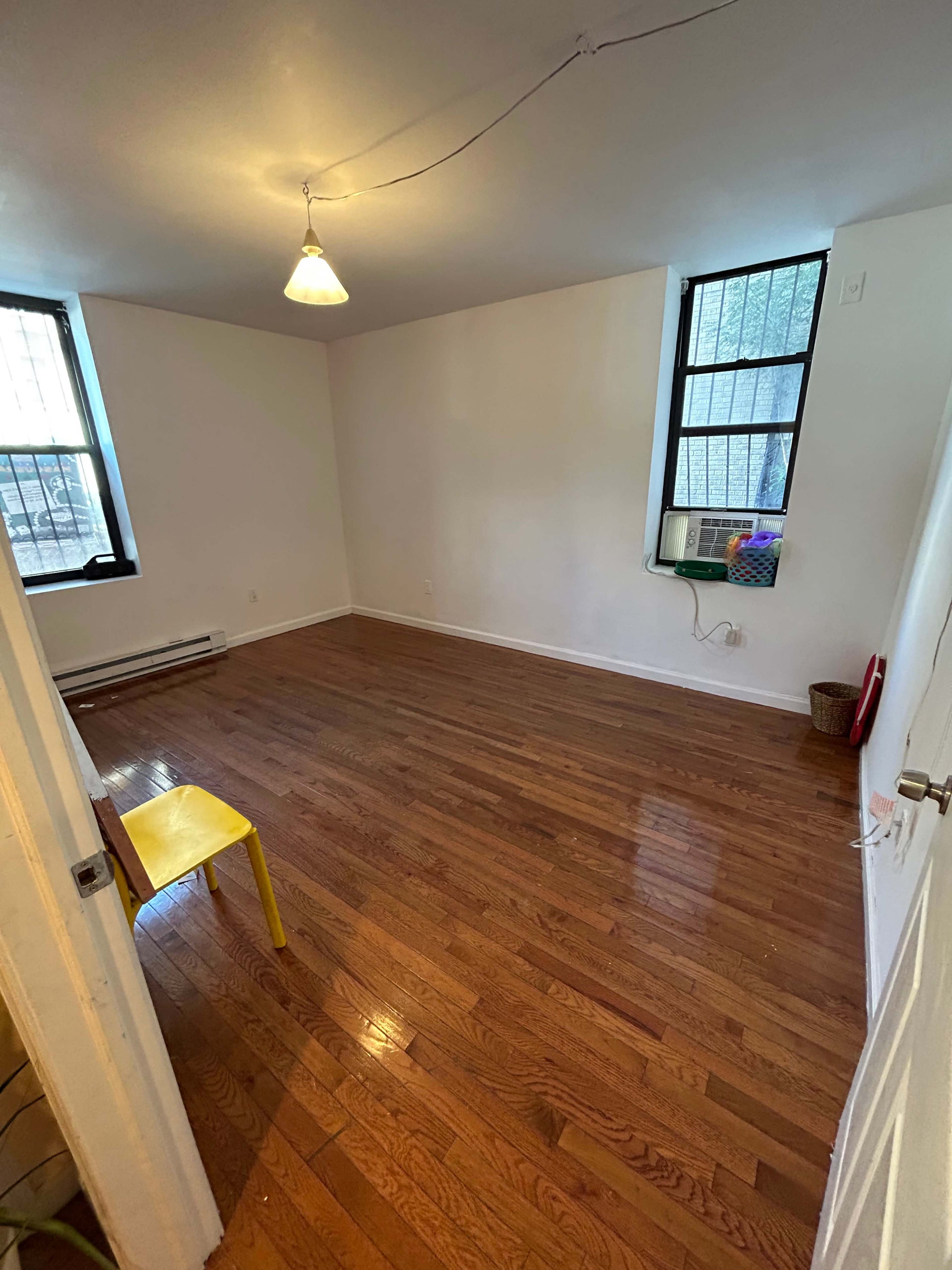 An empty room with hardwood floors, two windows, and a single yellow chair.