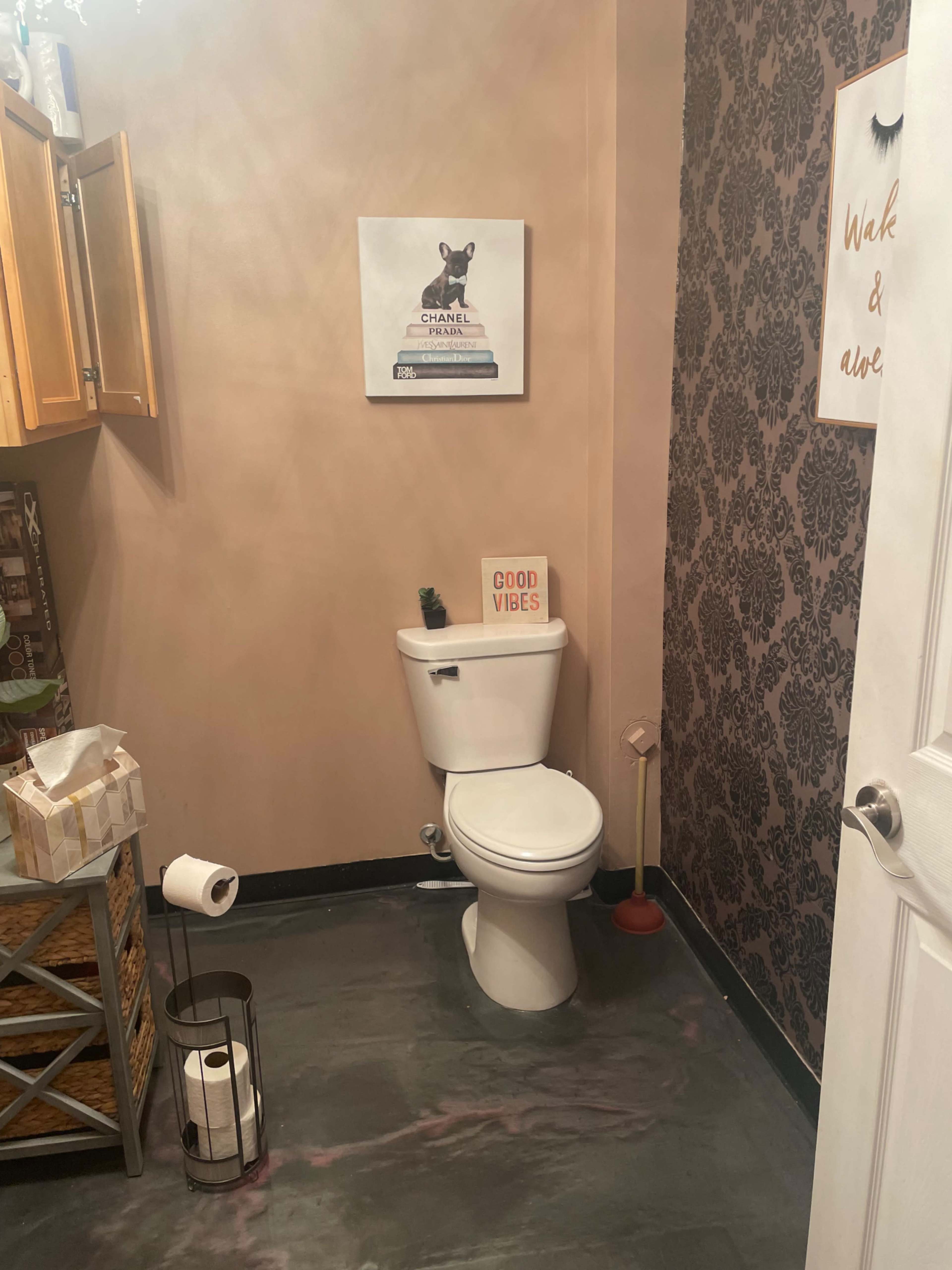 A small bathroom with a toilet, a decorative wall featuring dark patterns, and a wall-mounted artwork above the toilet.