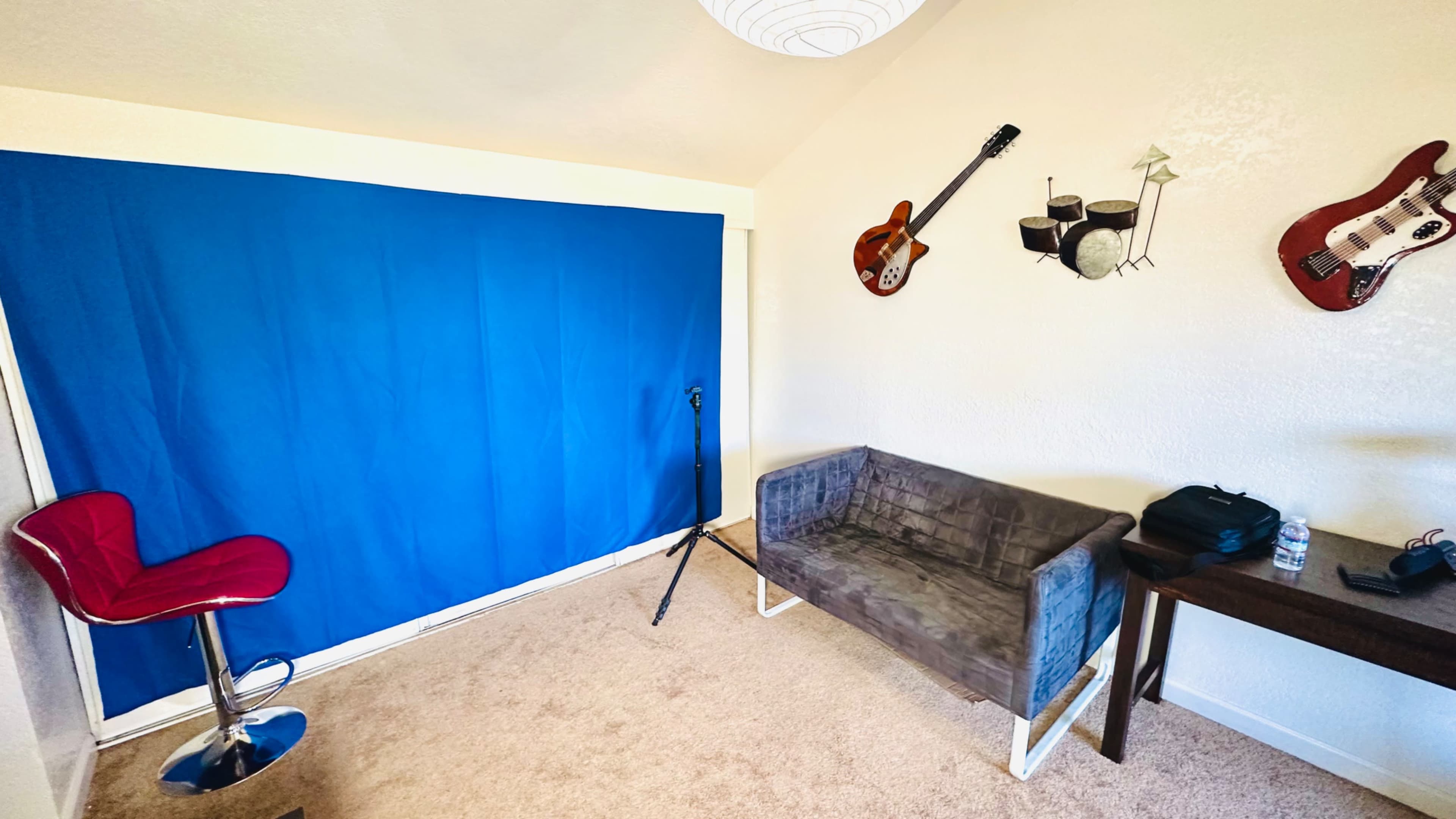 A small room featuring a blue backdrop, a gray sofa, a microphone stand, and three hanging musical instruments on the wall.