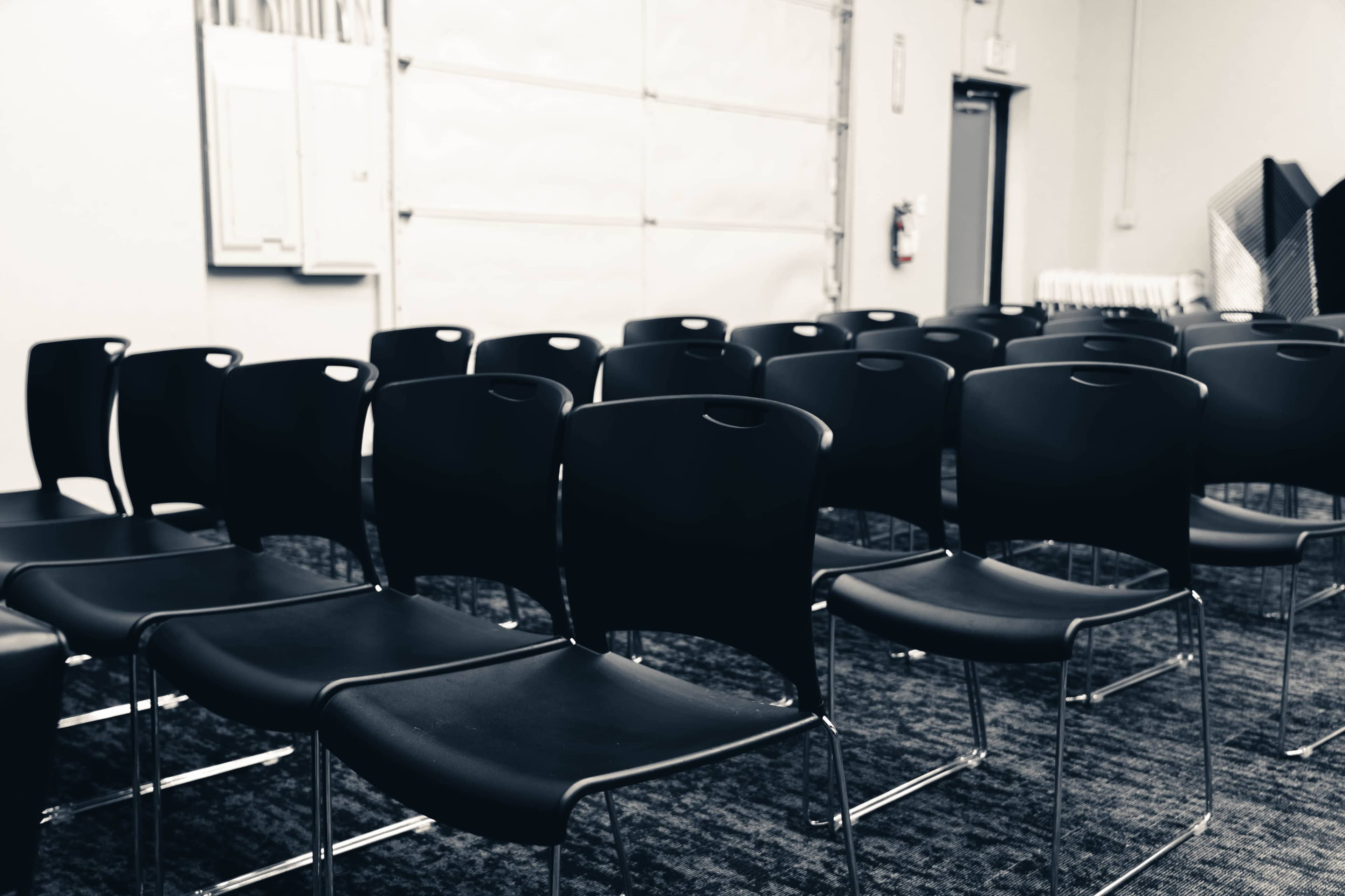 The image shows a row of black chairs arranged in a room with a textured carpet.