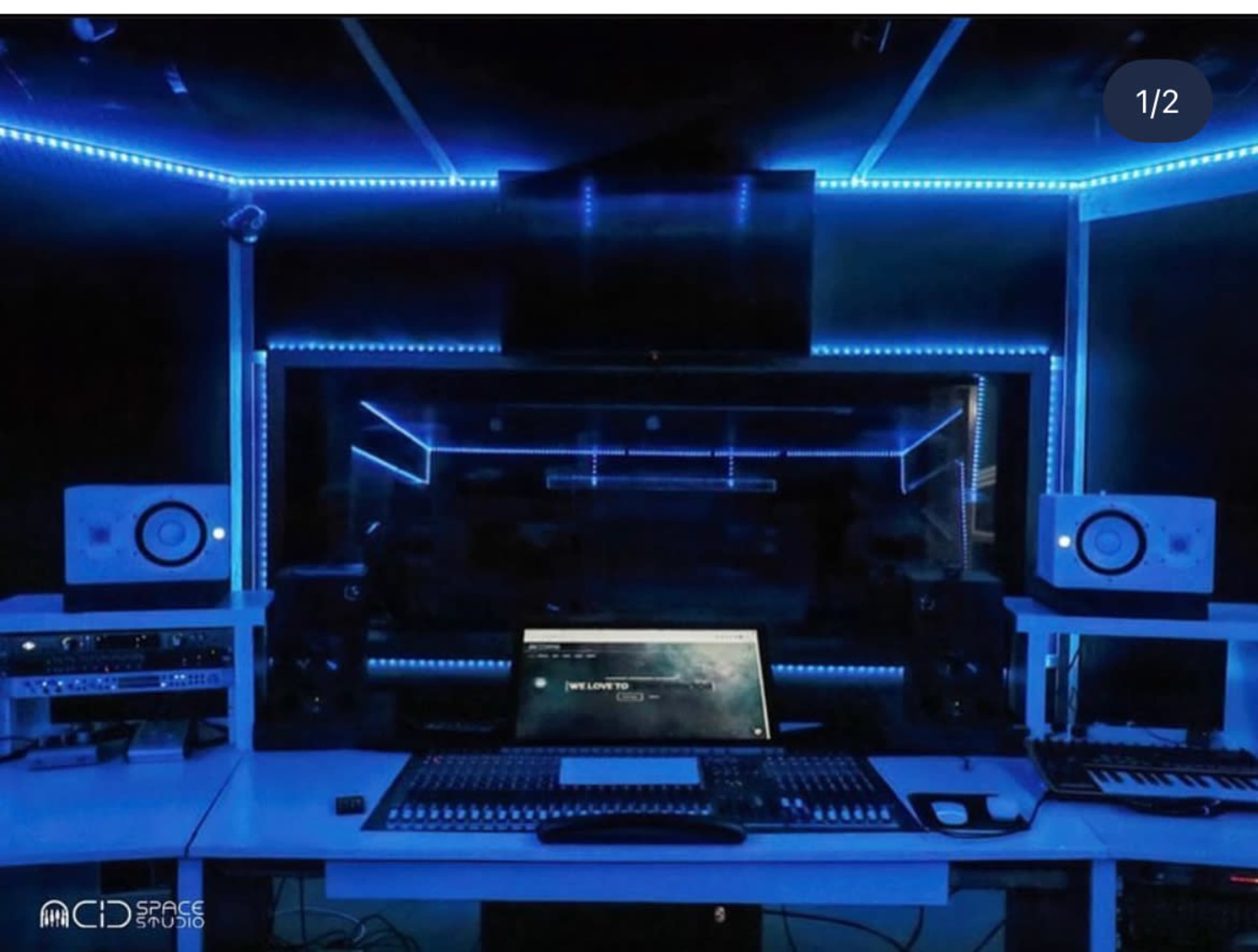 The image shows a modern music studio with blue LED lighting, featuring a large computer monitor, mixing console, and audio equipment.