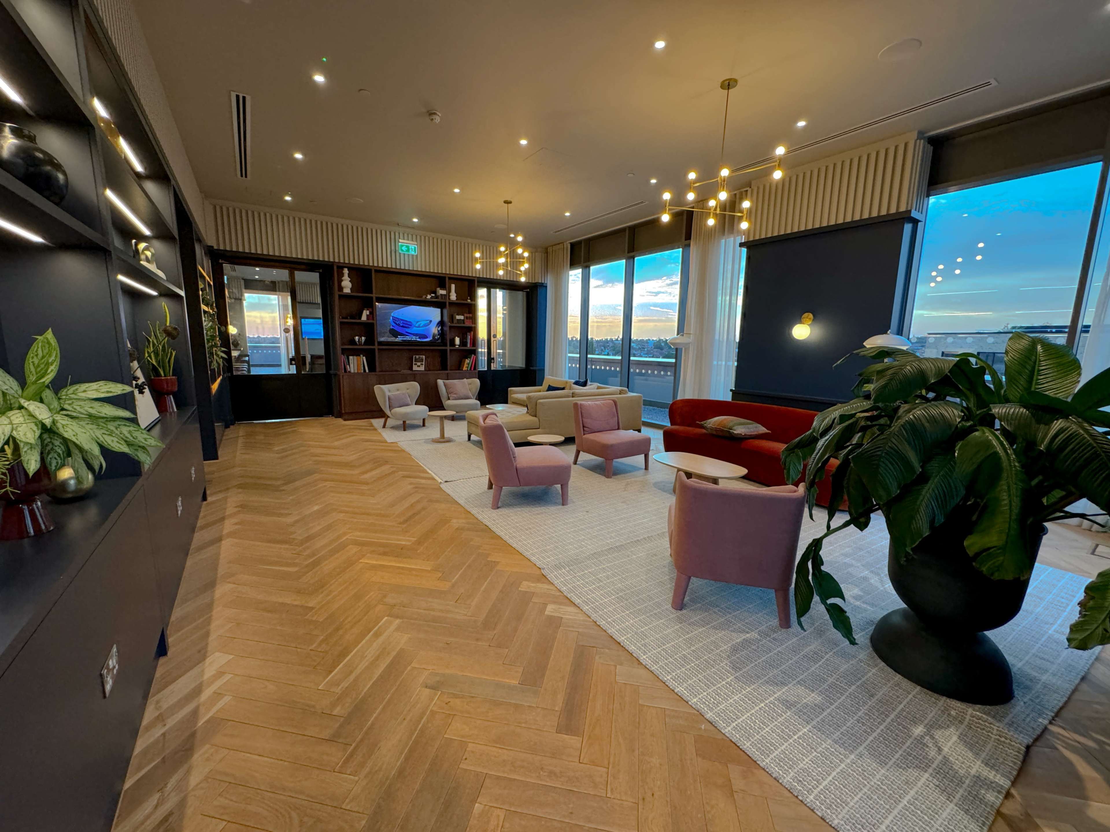 A modern lounge area with a mix of seating, plants, and large windows overlooking a scenic view.