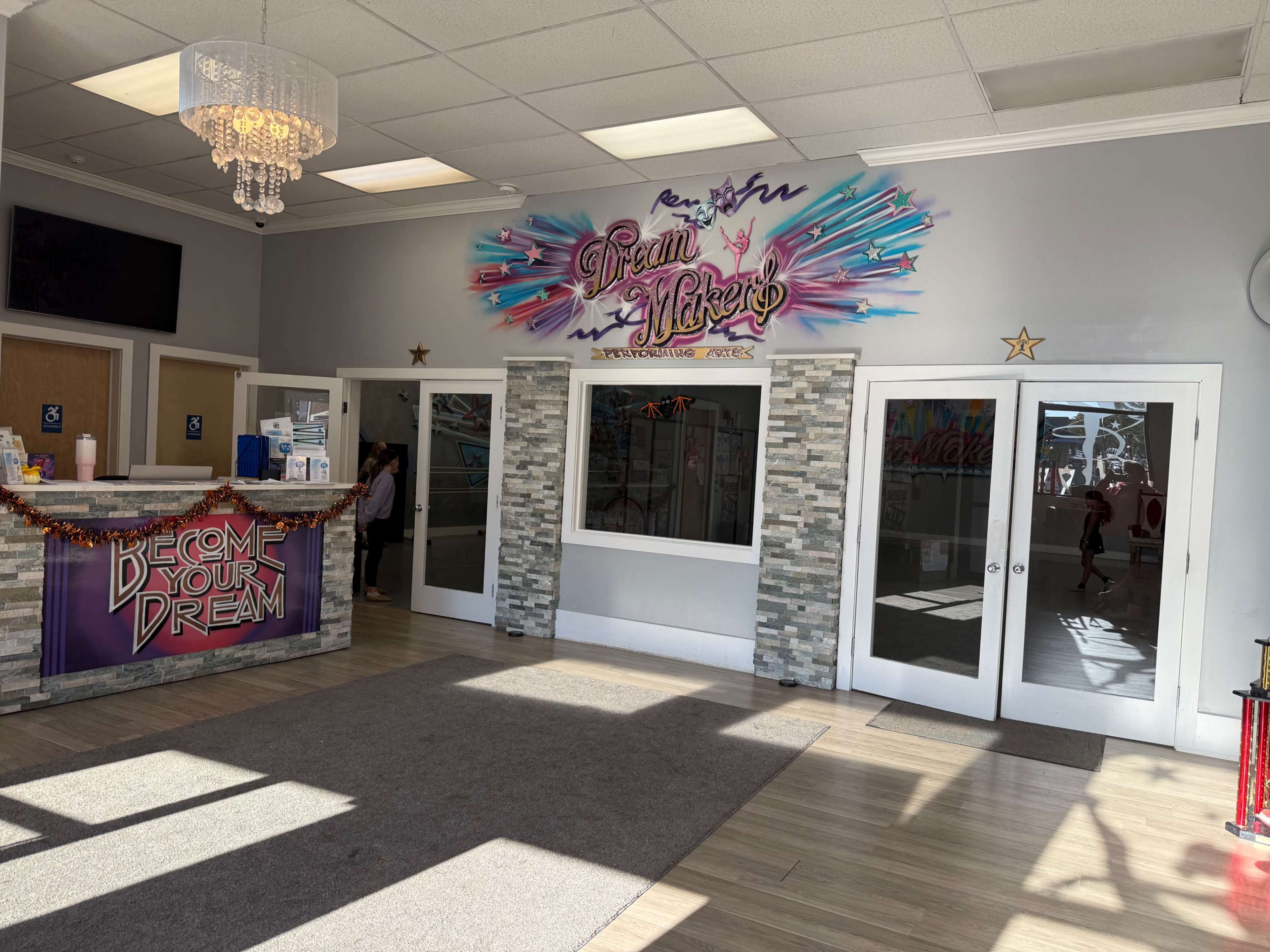 The interior of a brightly lit reception area features a front desk with colorful signage and a large, decorative mural above.