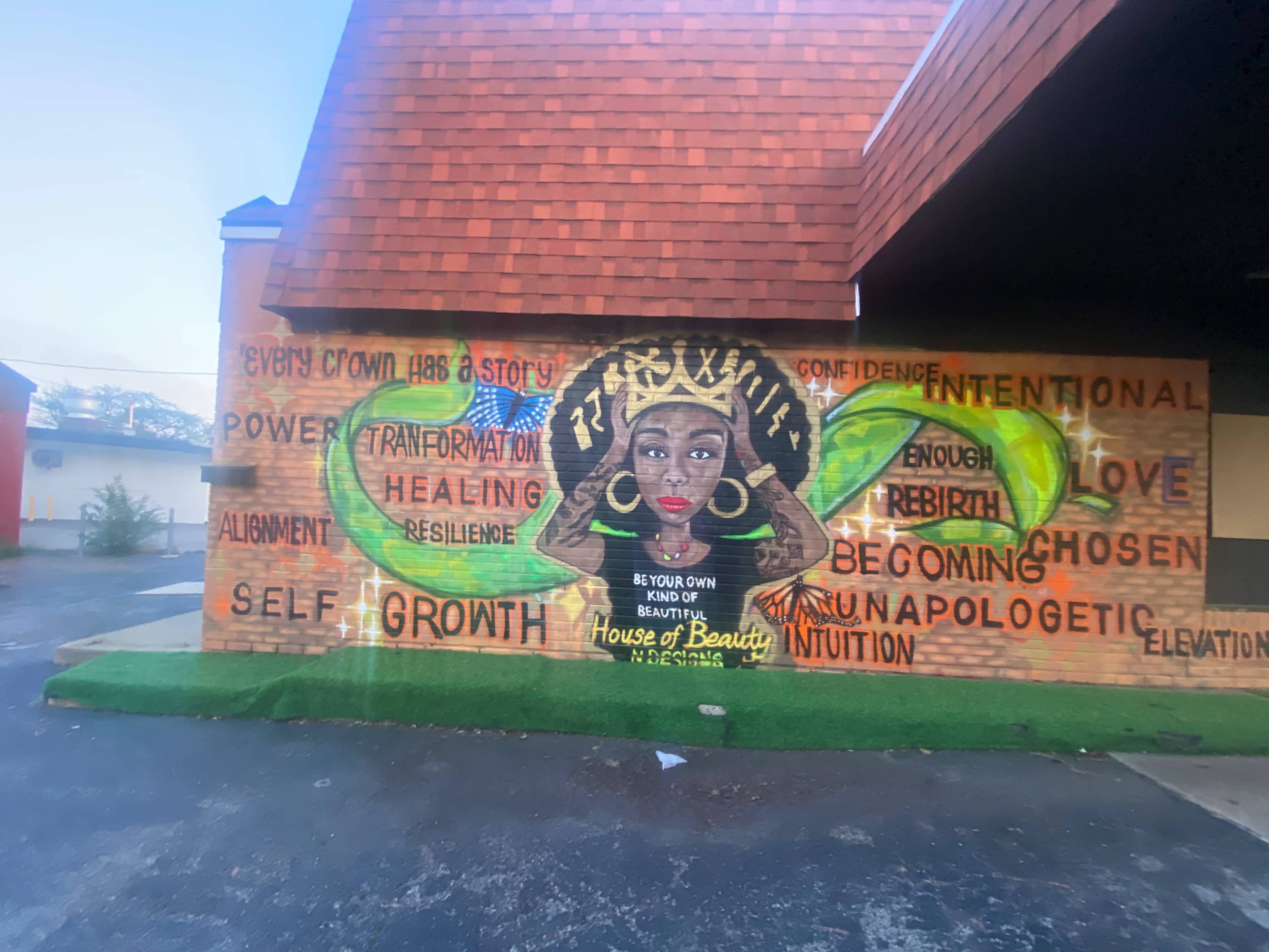 The image features a vibrant mural of a woman with an elaborate crown, surrounded by words such as "growth," "beauty," and "healing" painted on the wall.