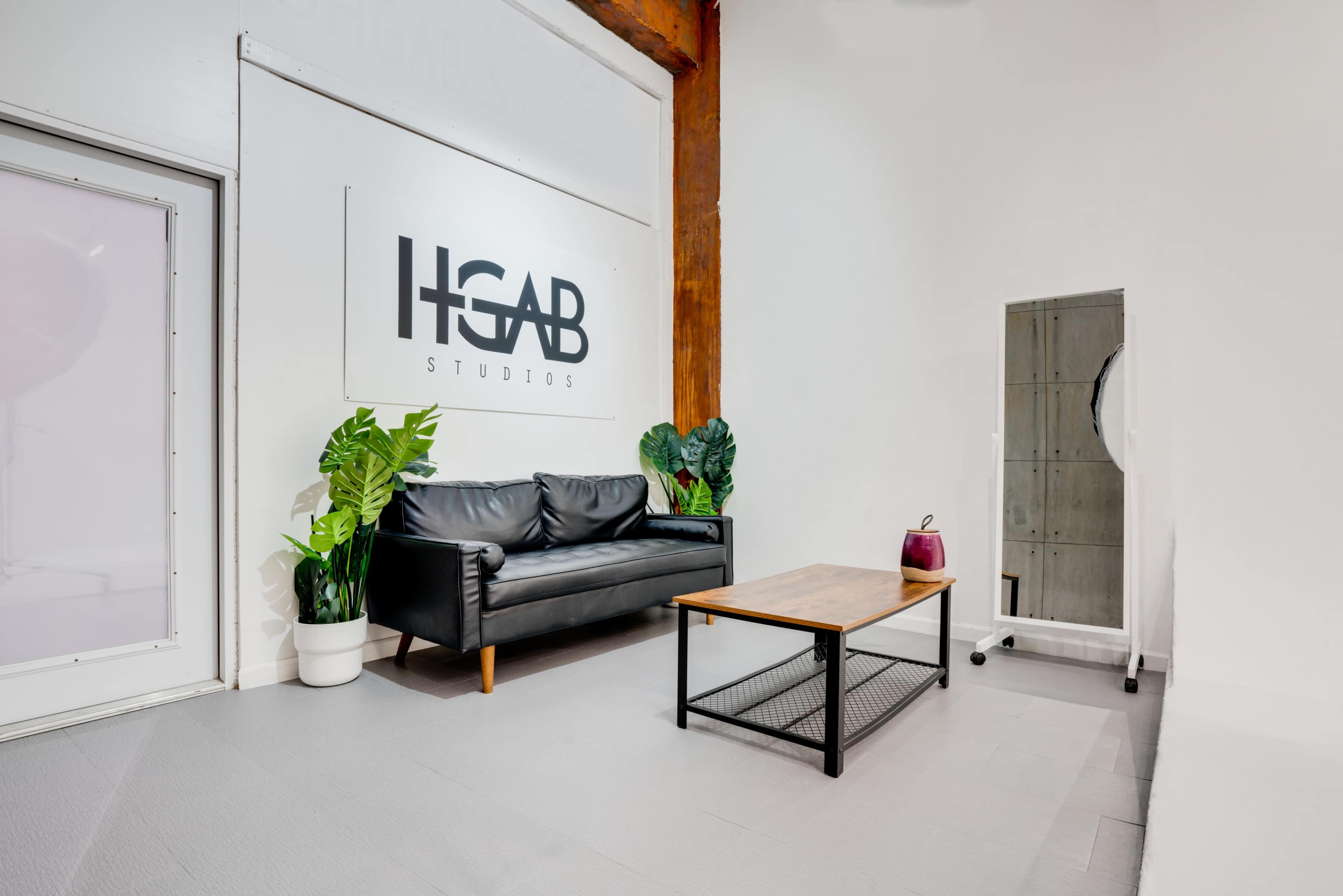 A modern studio space with a black couch, a wooden coffee table, and a wall displaying the logo "HGAB Studios."
