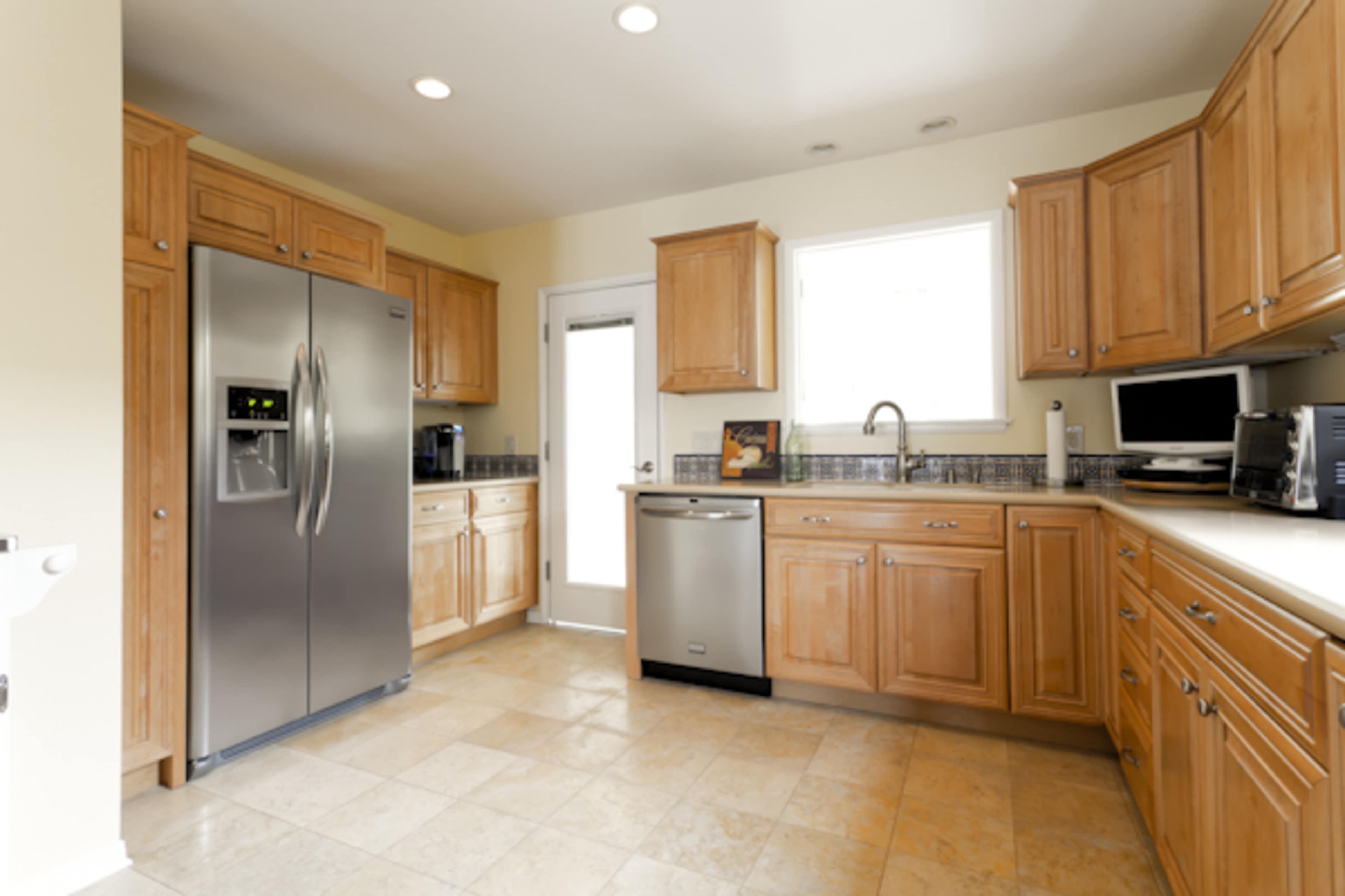 The kitchen features wooden cabinetry, stainless steel appliances, and a tiled floor with a door leading to the outside.