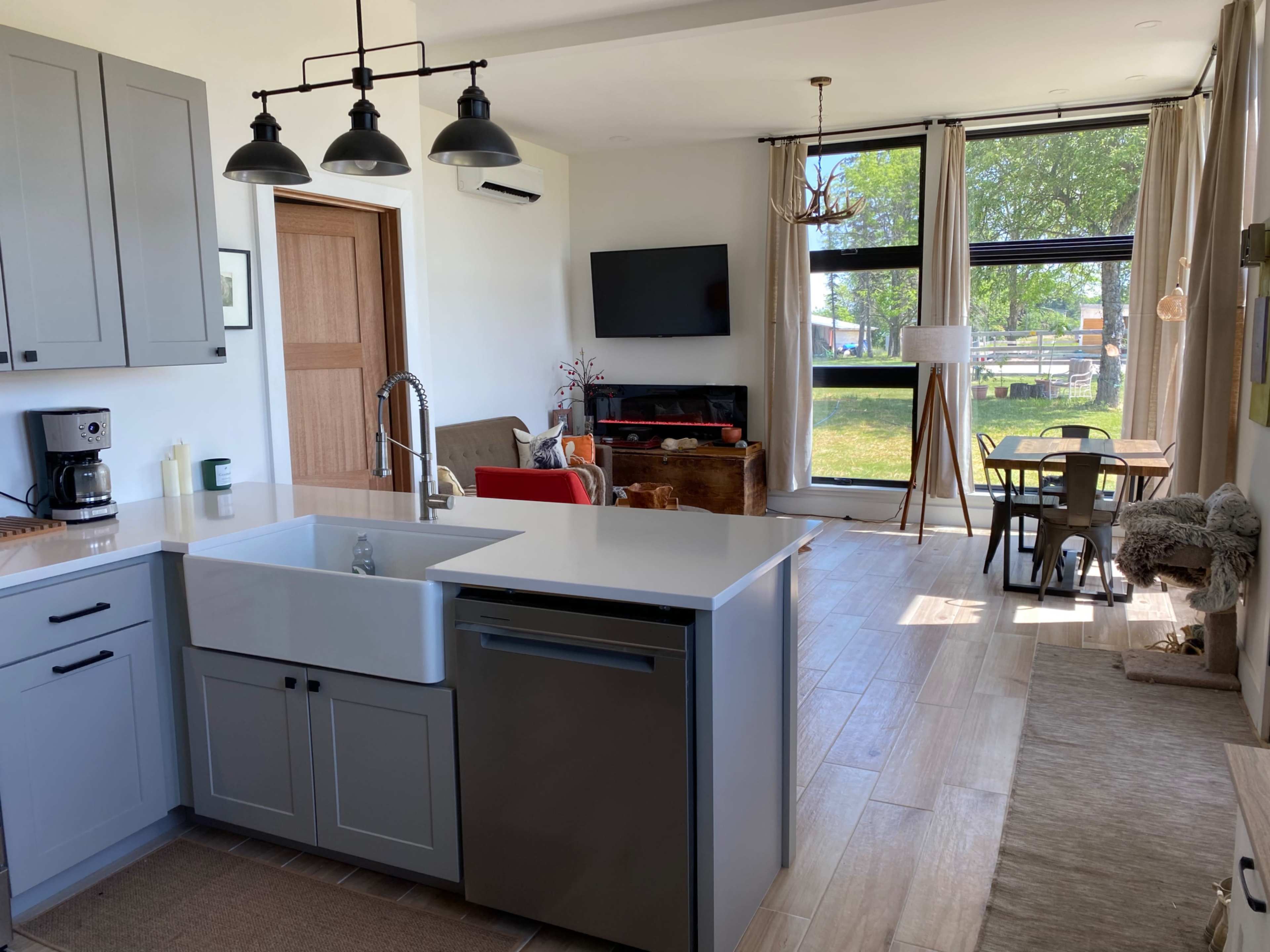 A modern kitchen seamlessly integrated with a living area, featuring a large island, a television, and a dining table by a window.