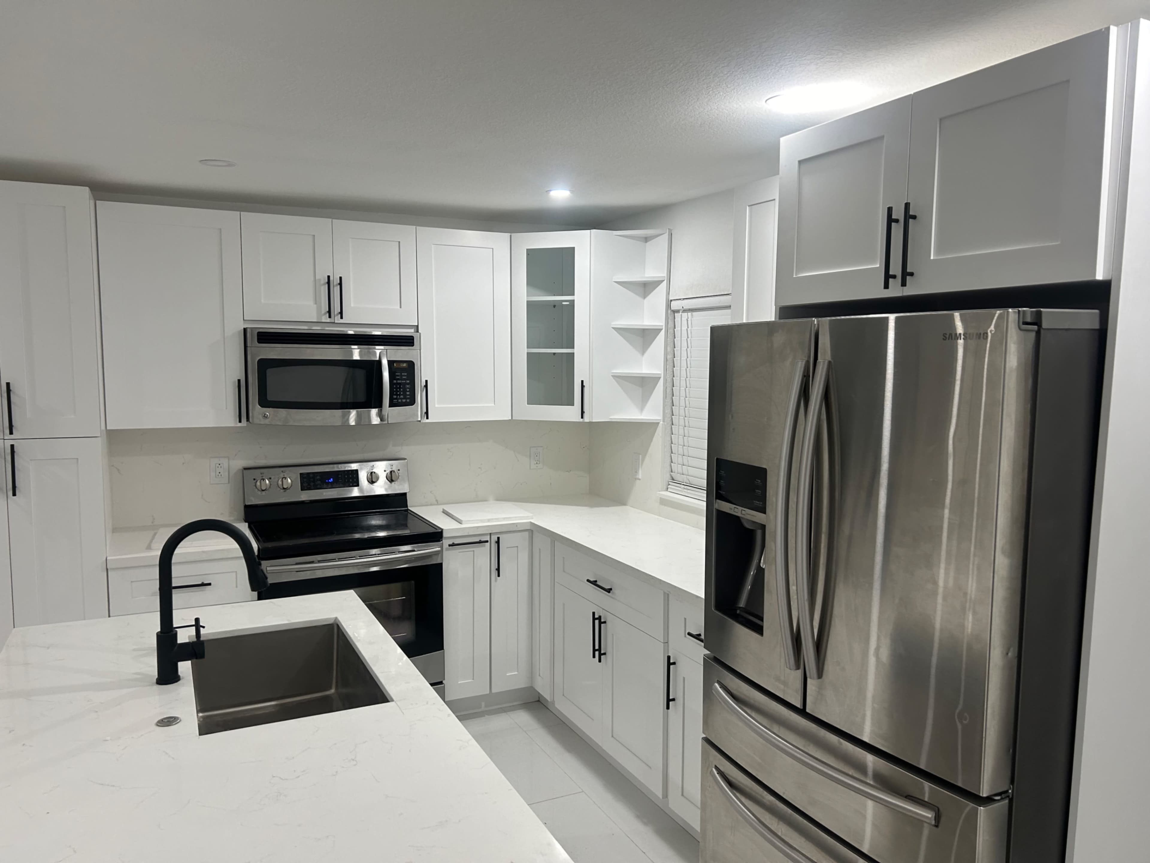 The image shows a modern kitchen with white cabinetry, stainless steel appliances, a sink in the island, and a light marble countertop.