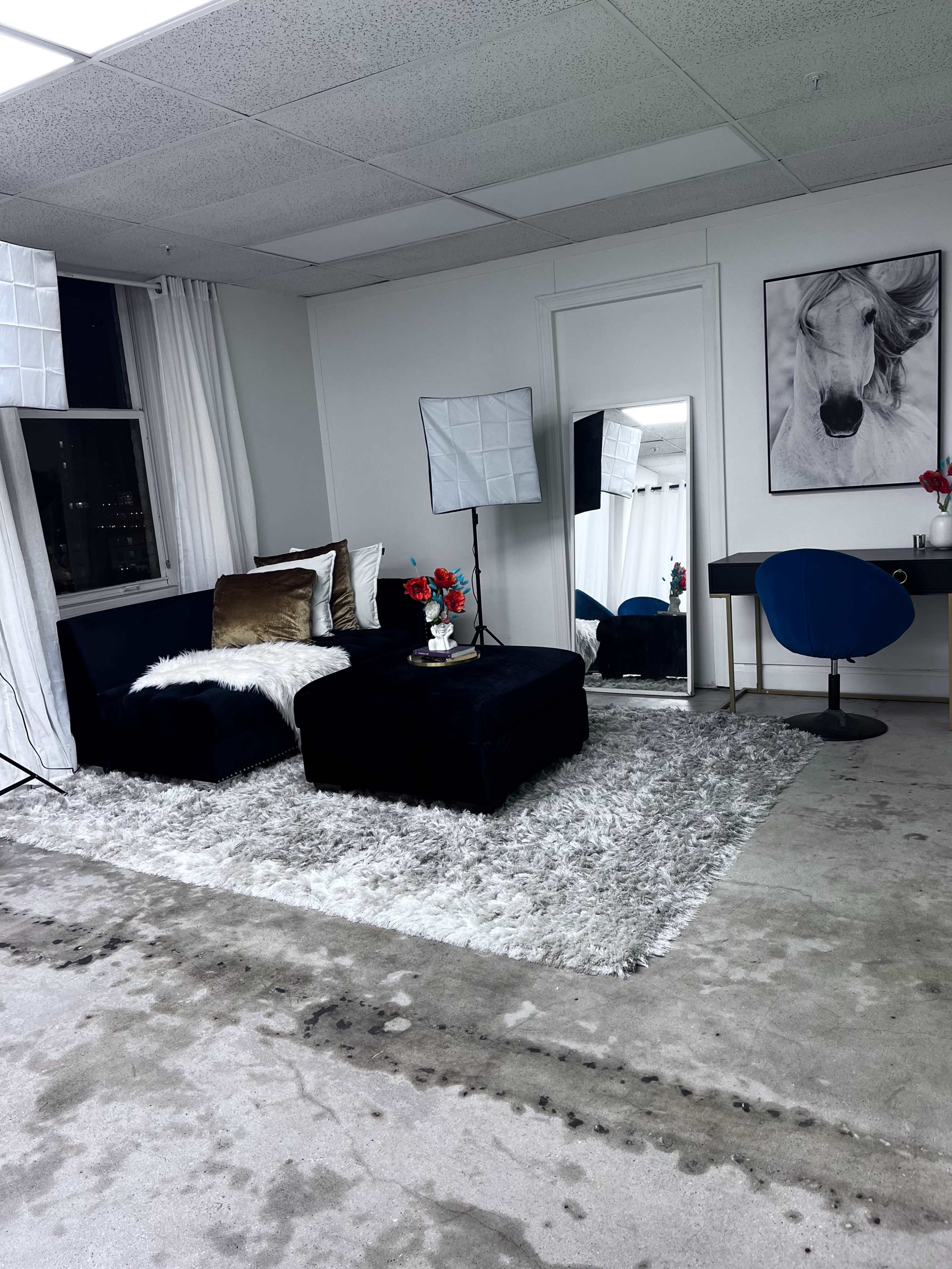 A modern living space with a dark sofa, a large mirror, and a table with a blue chair, set against a backdrop of large windows and soft lighting.