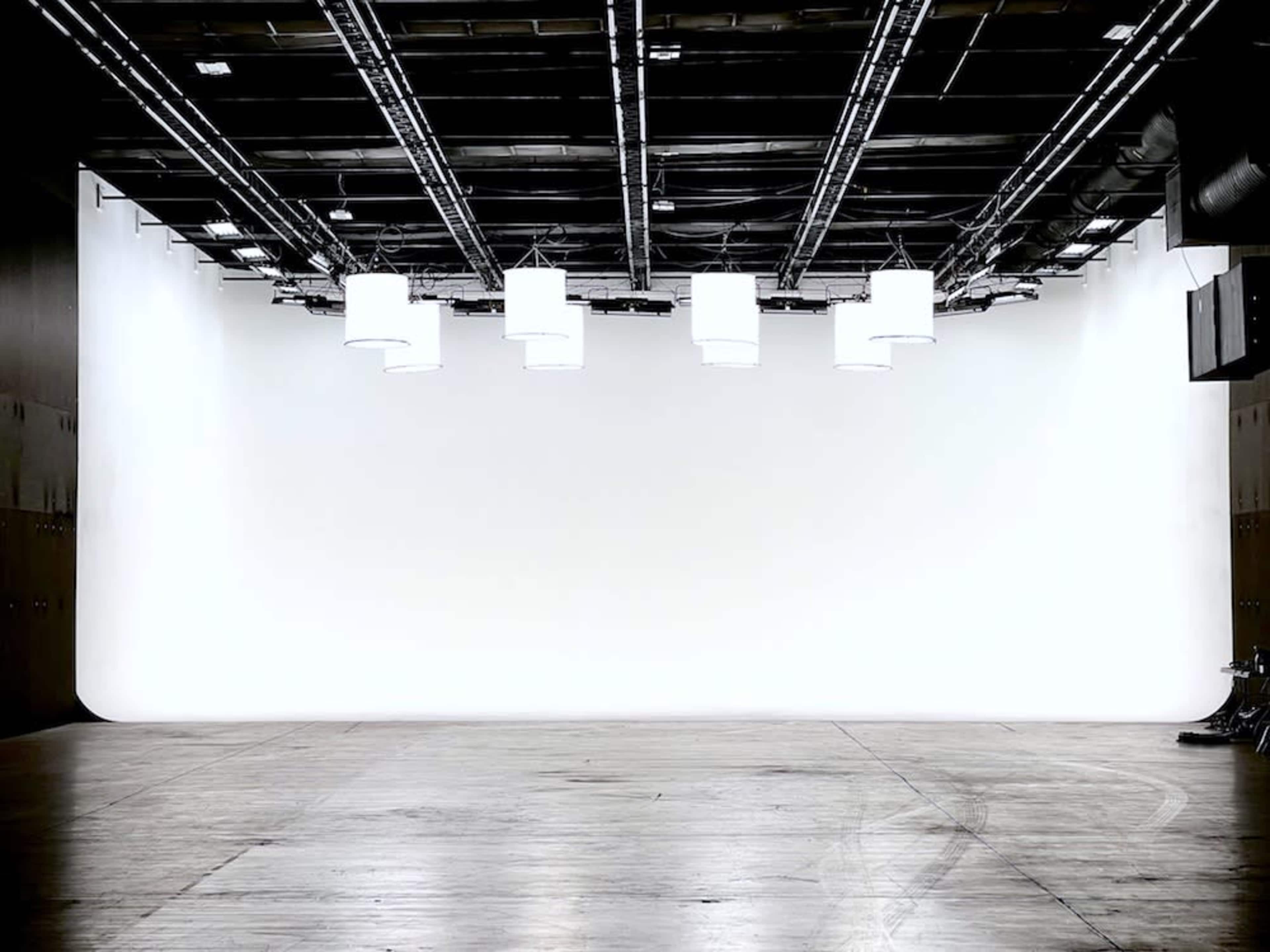An empty studio space features a plain white backdrop and overhead lighting fixtures.