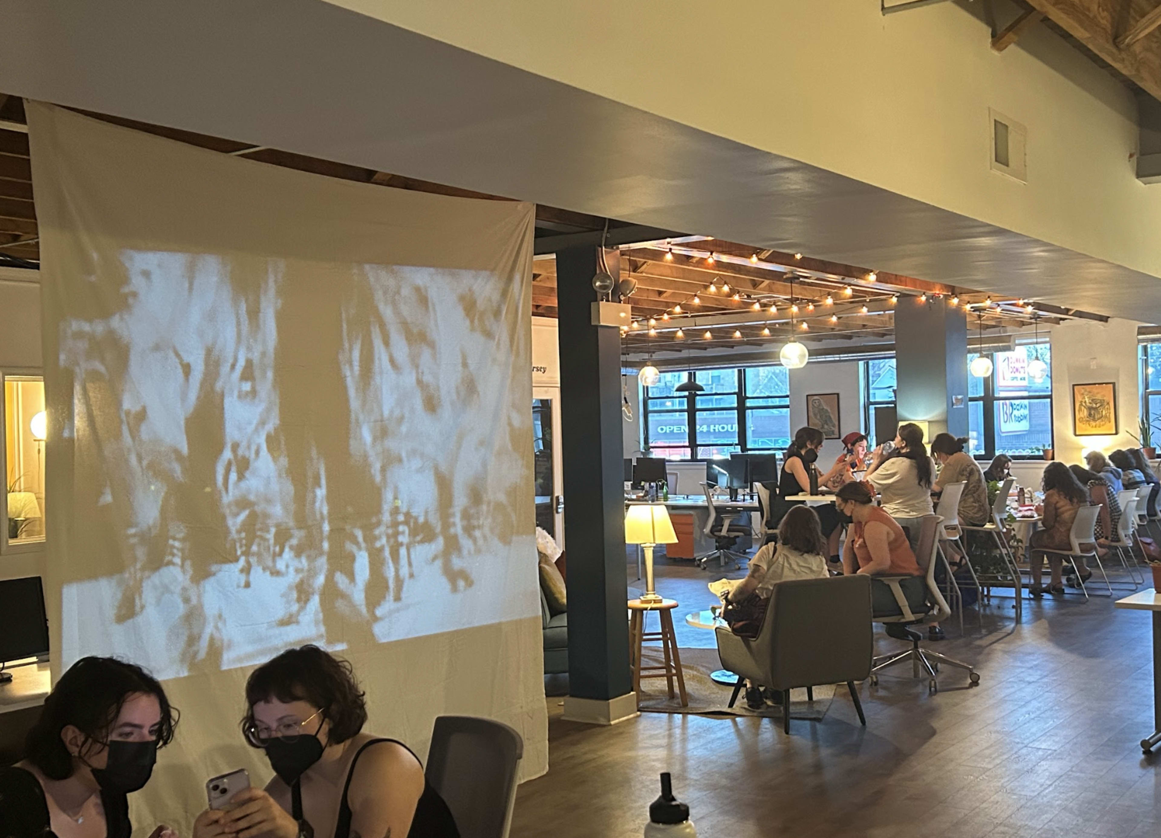 A busy café with patrons sitting at tables and a vintage film projected on a white sheet.