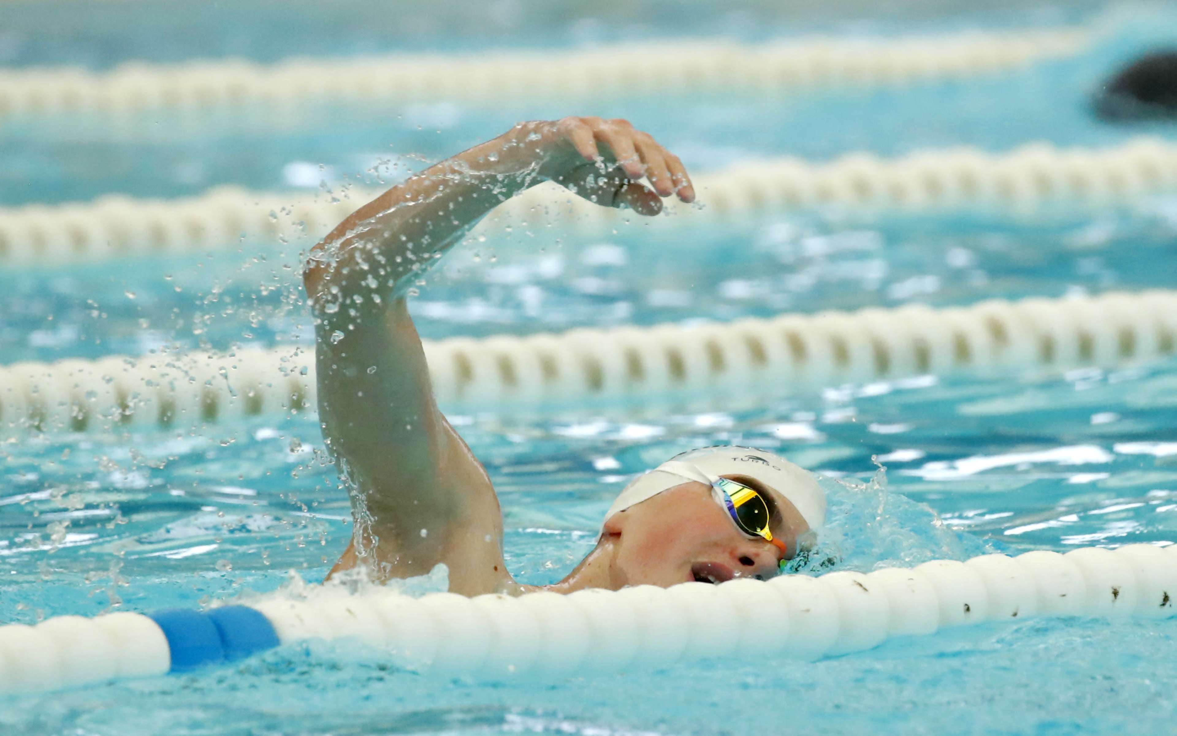 A swimmer performs the freestyle stroke in a pool, splashing water as they reach forward with one arm.