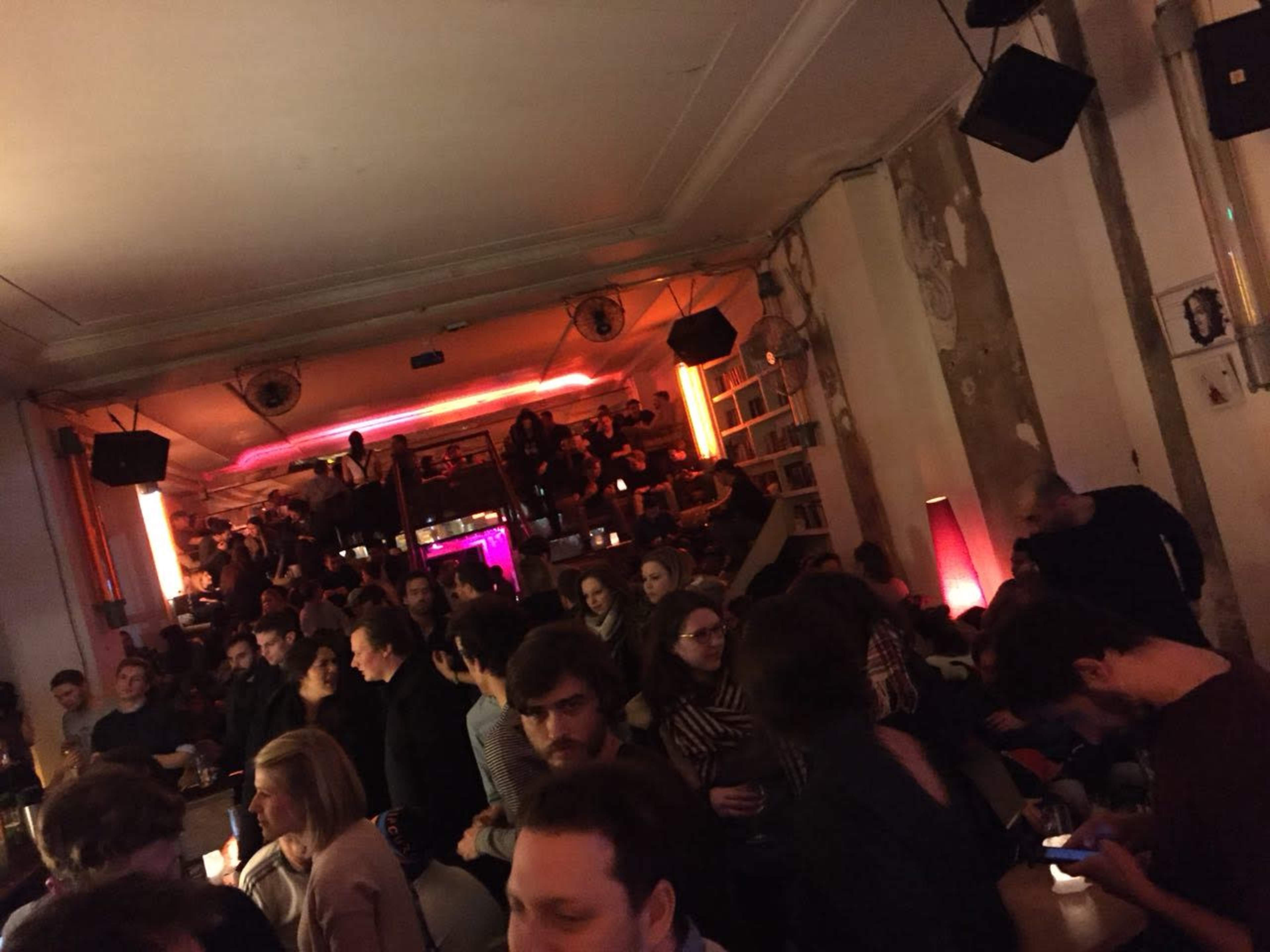 A crowded bar scene shows people sitting and standing, with dim lighting and a colorful backlit area.