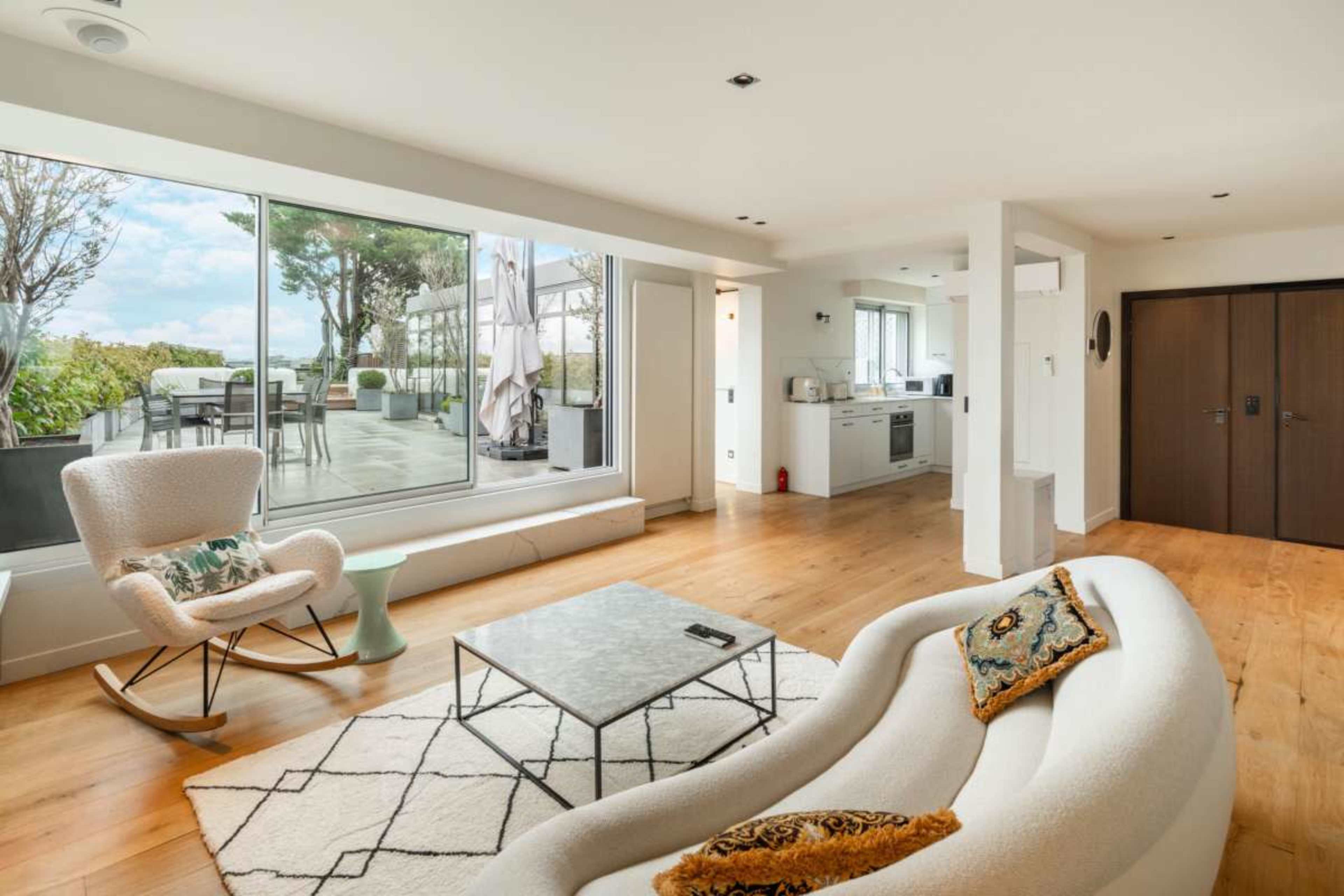 The image depicts a modern, open-concept living space featuring a sleek curved sofa, a marble coffee table, and large windows that bring in natural light.