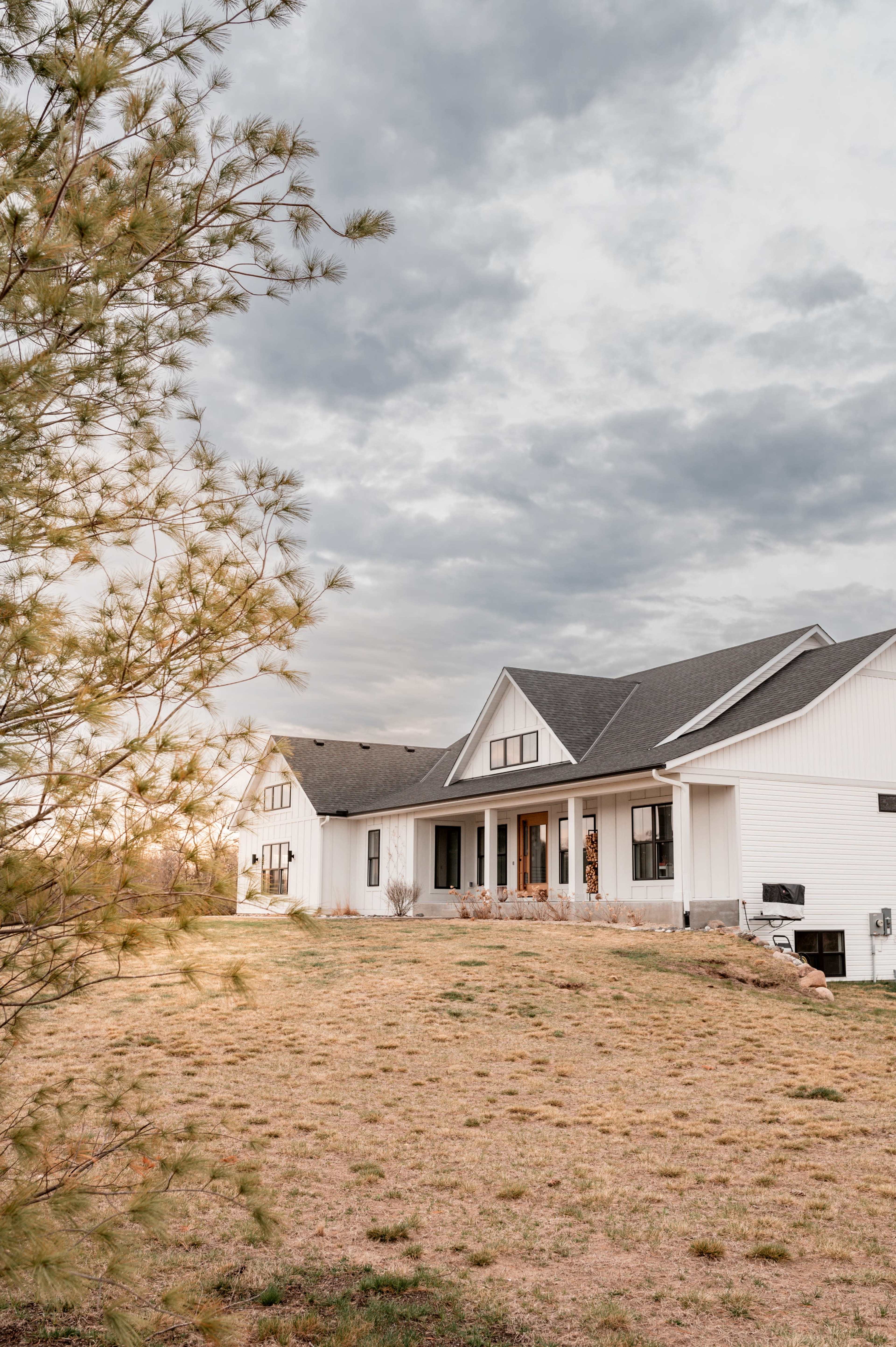 A large white house with a gray roof is situated on a grassy hillside under an overcast sky.