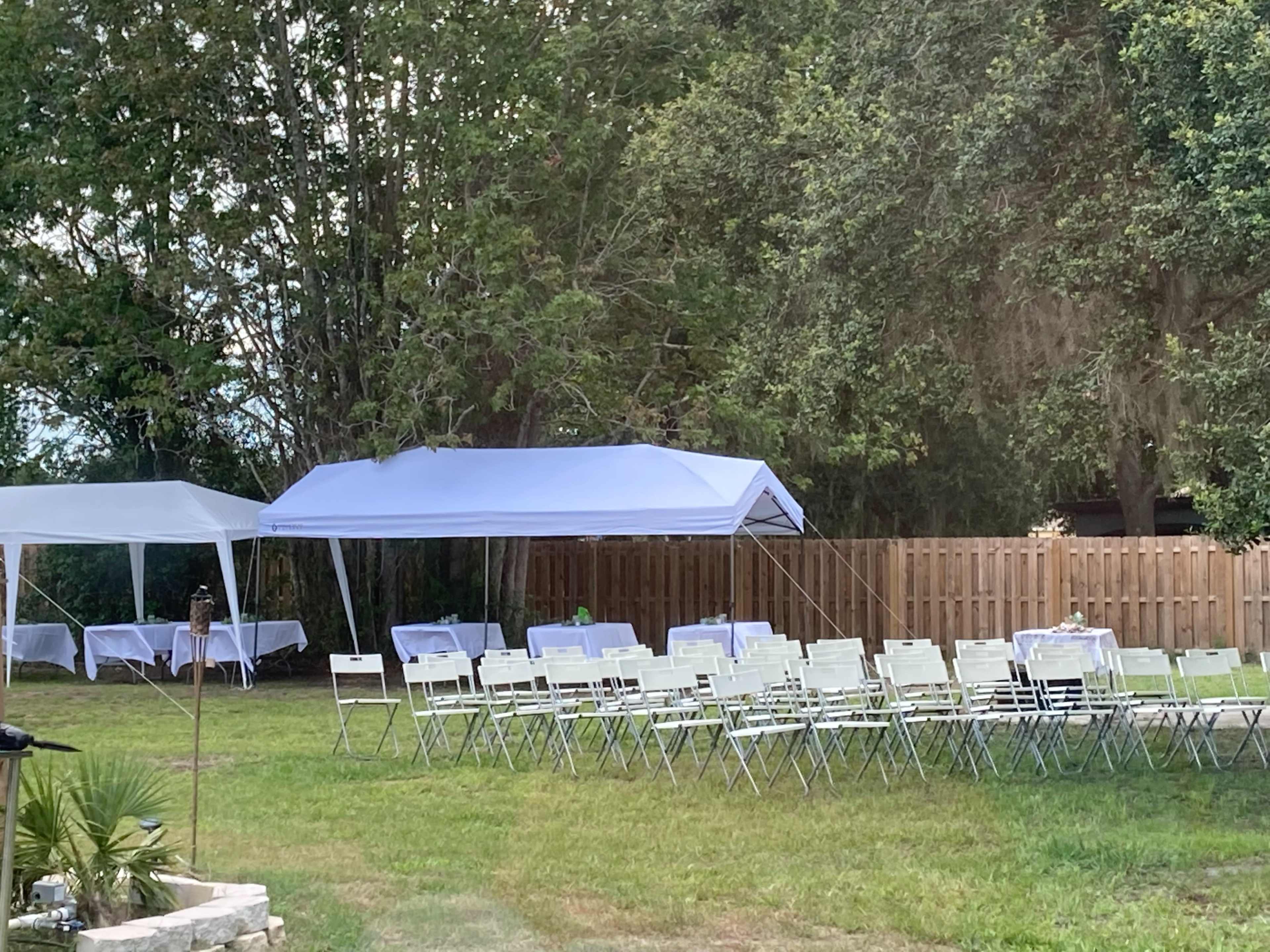A spacious outdoor area set up for an event, featuring two white canopies and rows of green folding chairs arranged on grass.