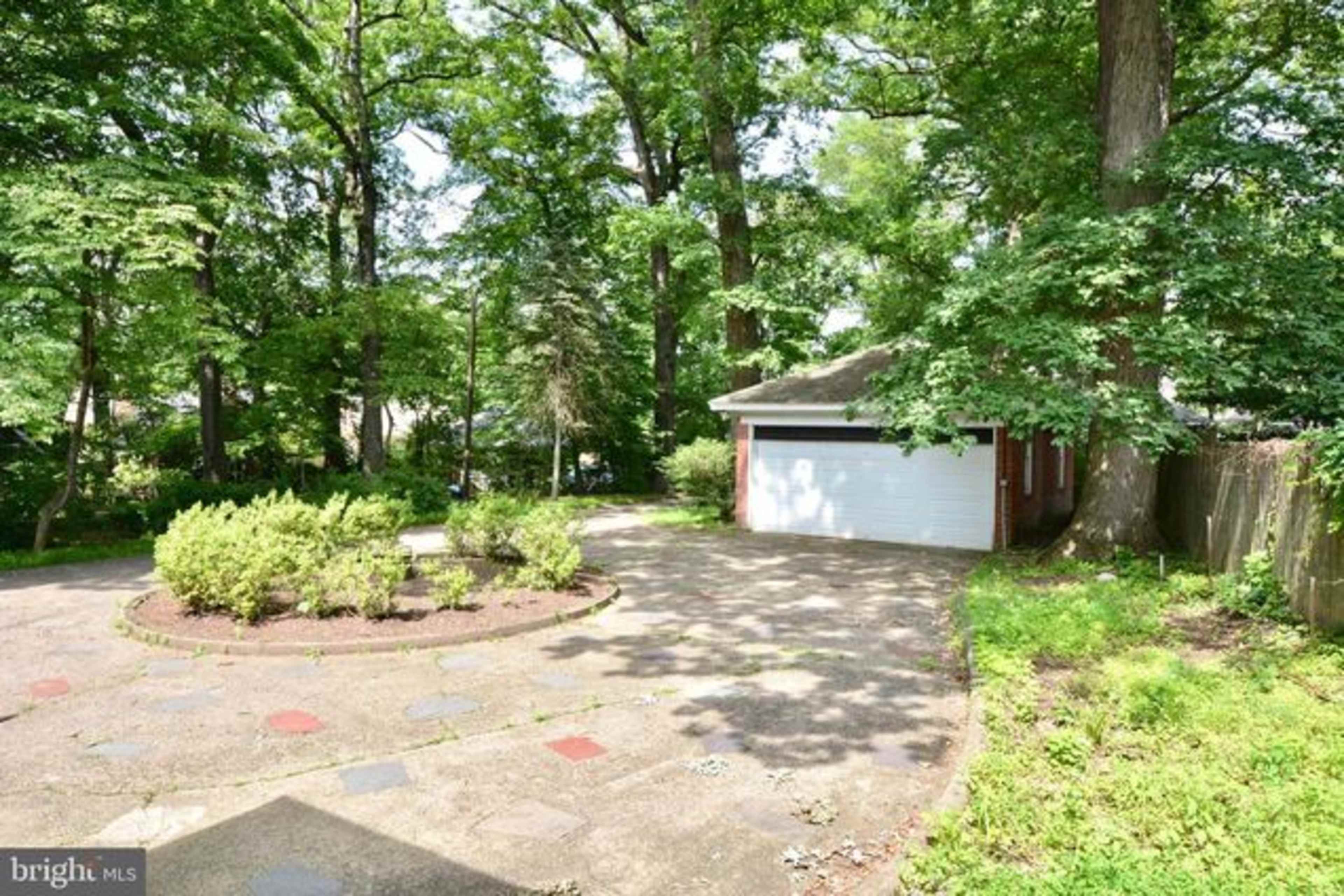A paved driveway leading to a garage surrounded by trees and shrubs.