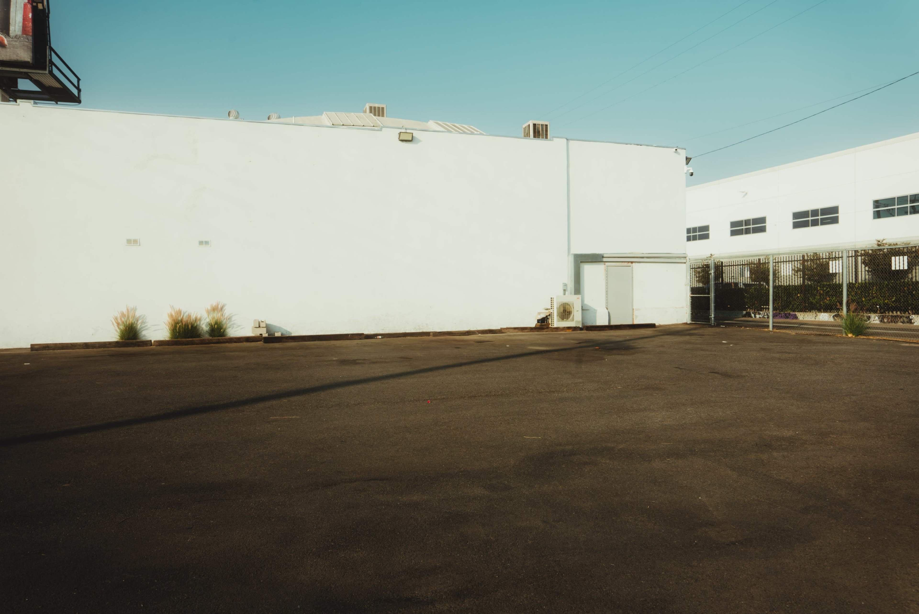 The image shows an empty parking lot with a pale blue wall and a small structure against it.