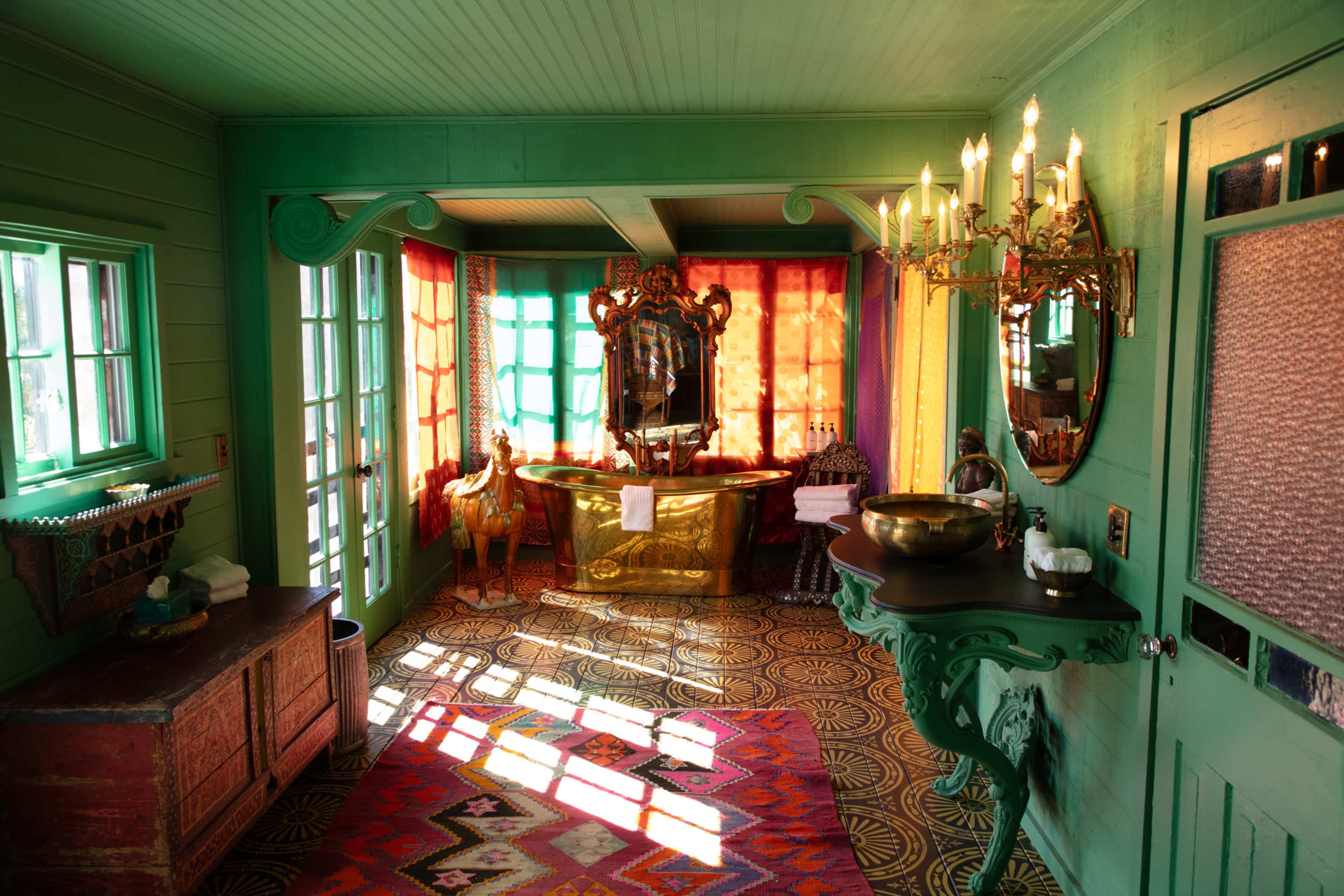 The image shows a brightly colored bathroom with green walls, a gold bathtub, and large windows casting patterned shadows on the floor.