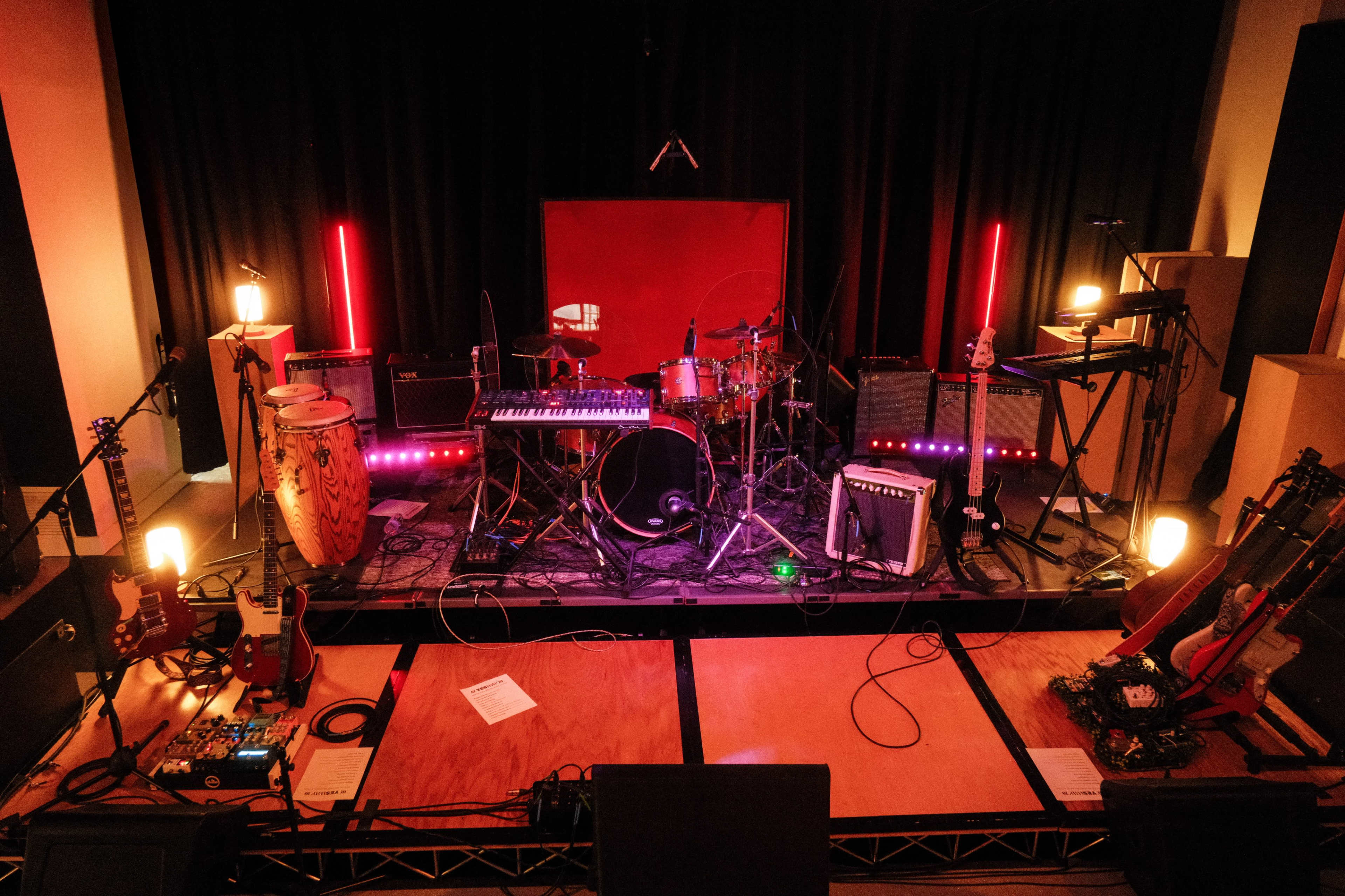 The image shows a concert stage setup with various musical instruments, including guitars, drums, keyboards, and amplifiers, illuminated by soft lighting.