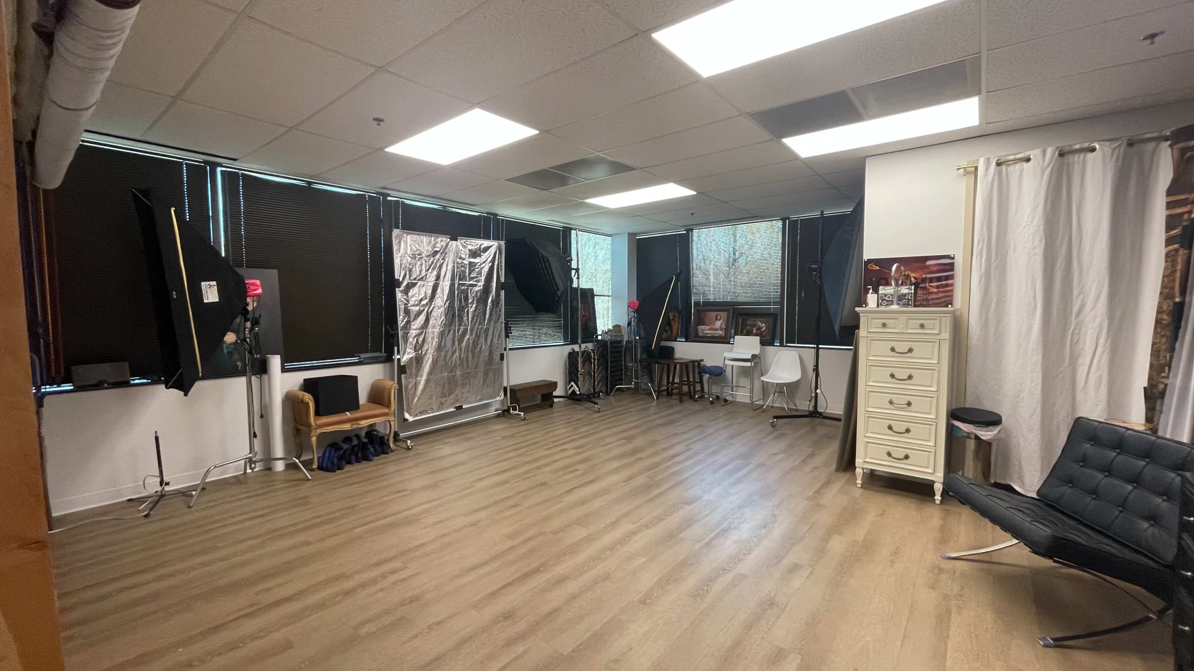 The image shows a spacious studio with hardwood flooring, large windows, and various photography equipment set up around the room.