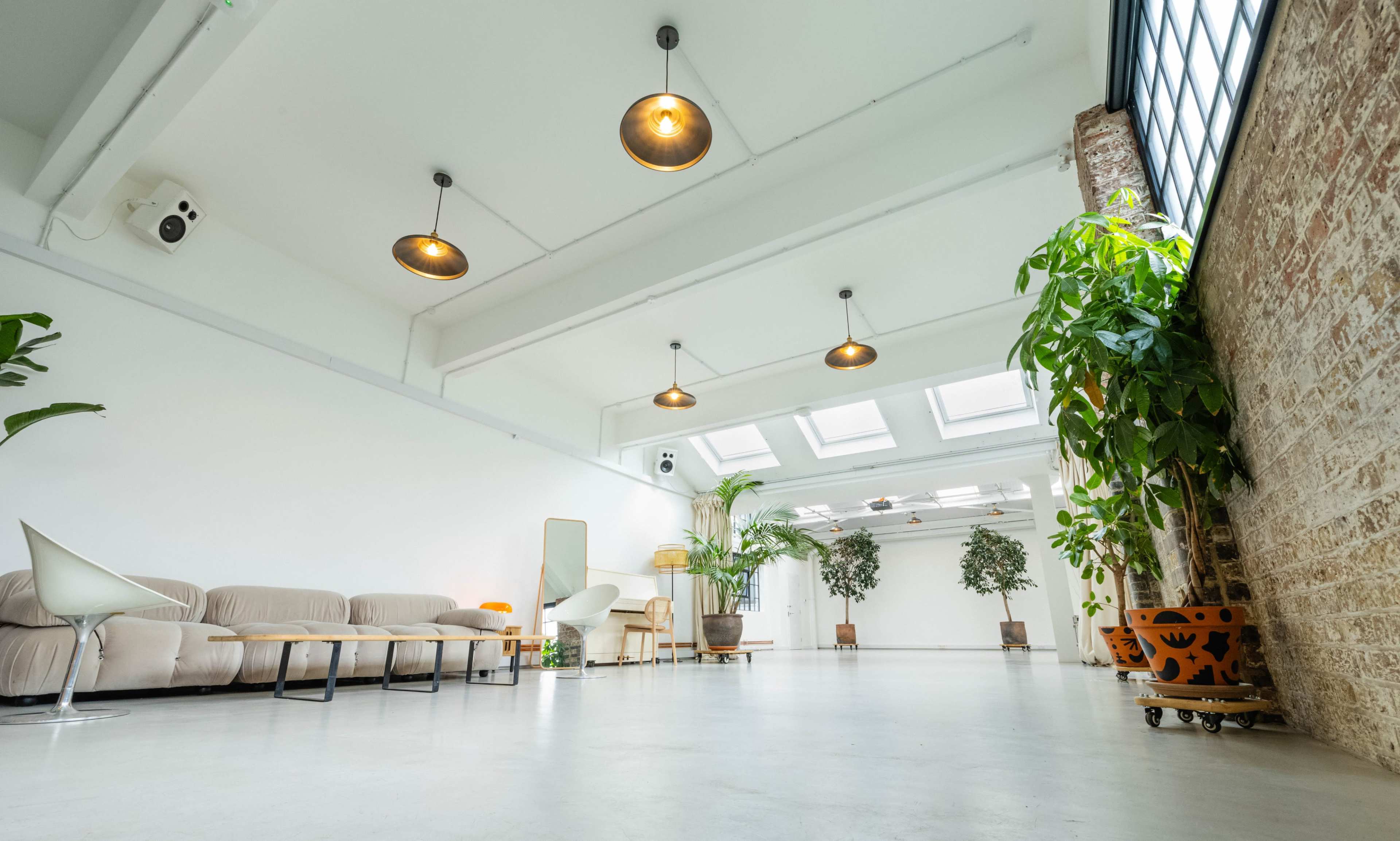 A spacious, minimalist room with a beige sofa, a wooden coffee table, potted plants, and large skylights.
