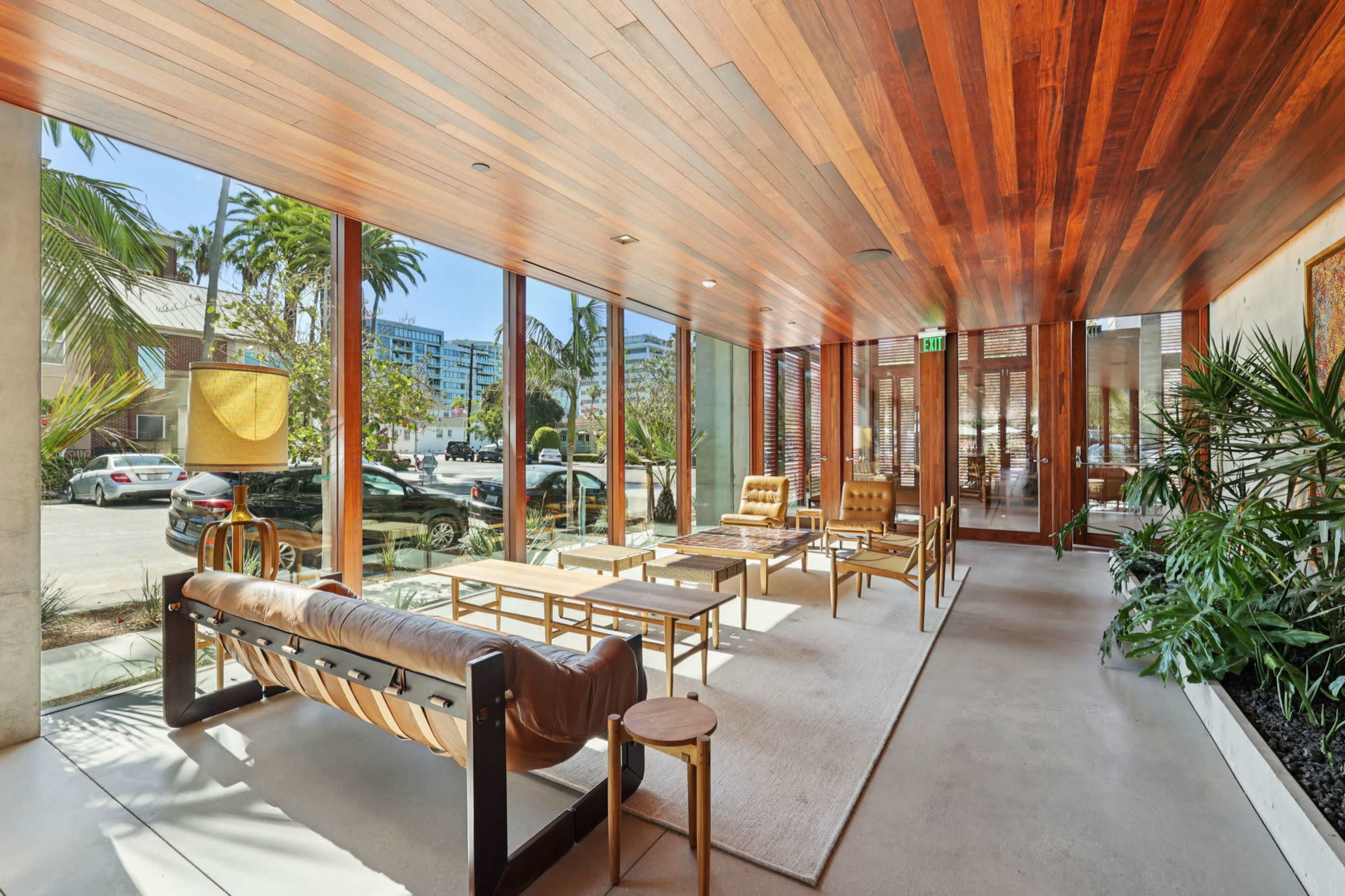 The image shows a modern lounge area with wooden paneling, large windows allowing natural light, and contemporary furniture.