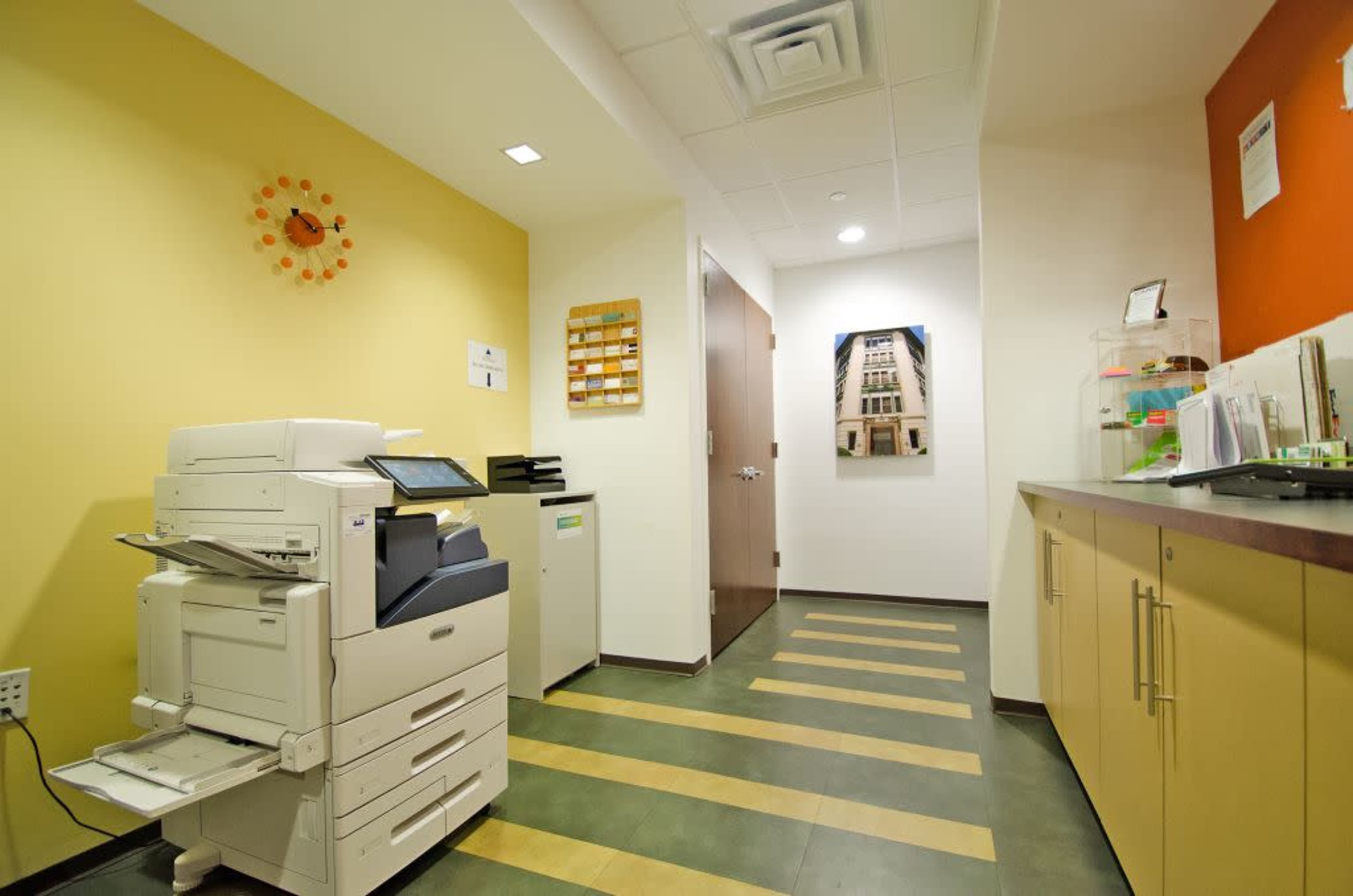 A hallway in an office featuring a printer, cabinets, and colorful walls.