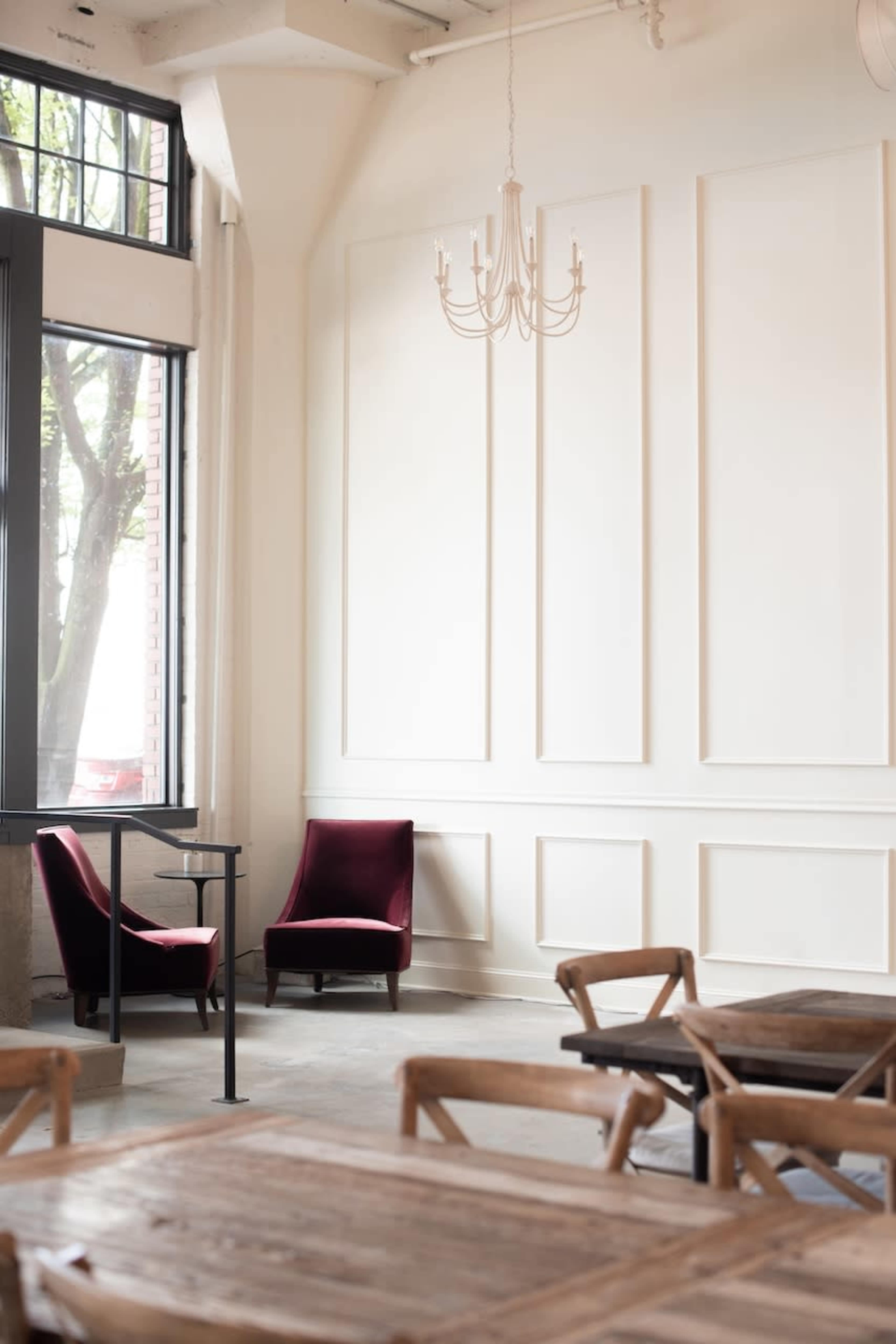 A bright room features two red chairs and a small table near large windows, with a chandelier suspended from the ceiling.