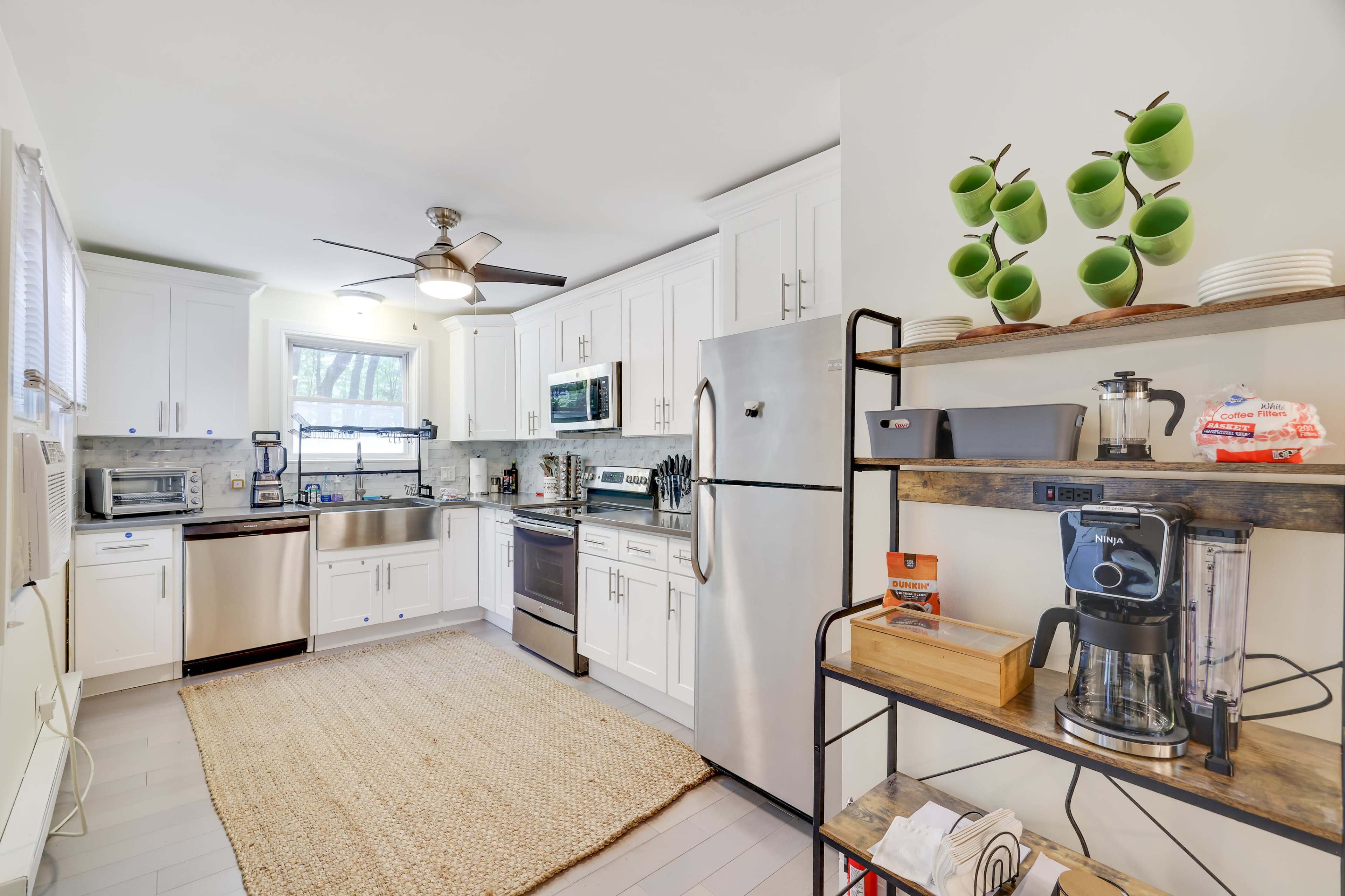 A modern kitchen equipped with stainless steel appliances, white cabinetry, and an open shelving unit with kitchenware.