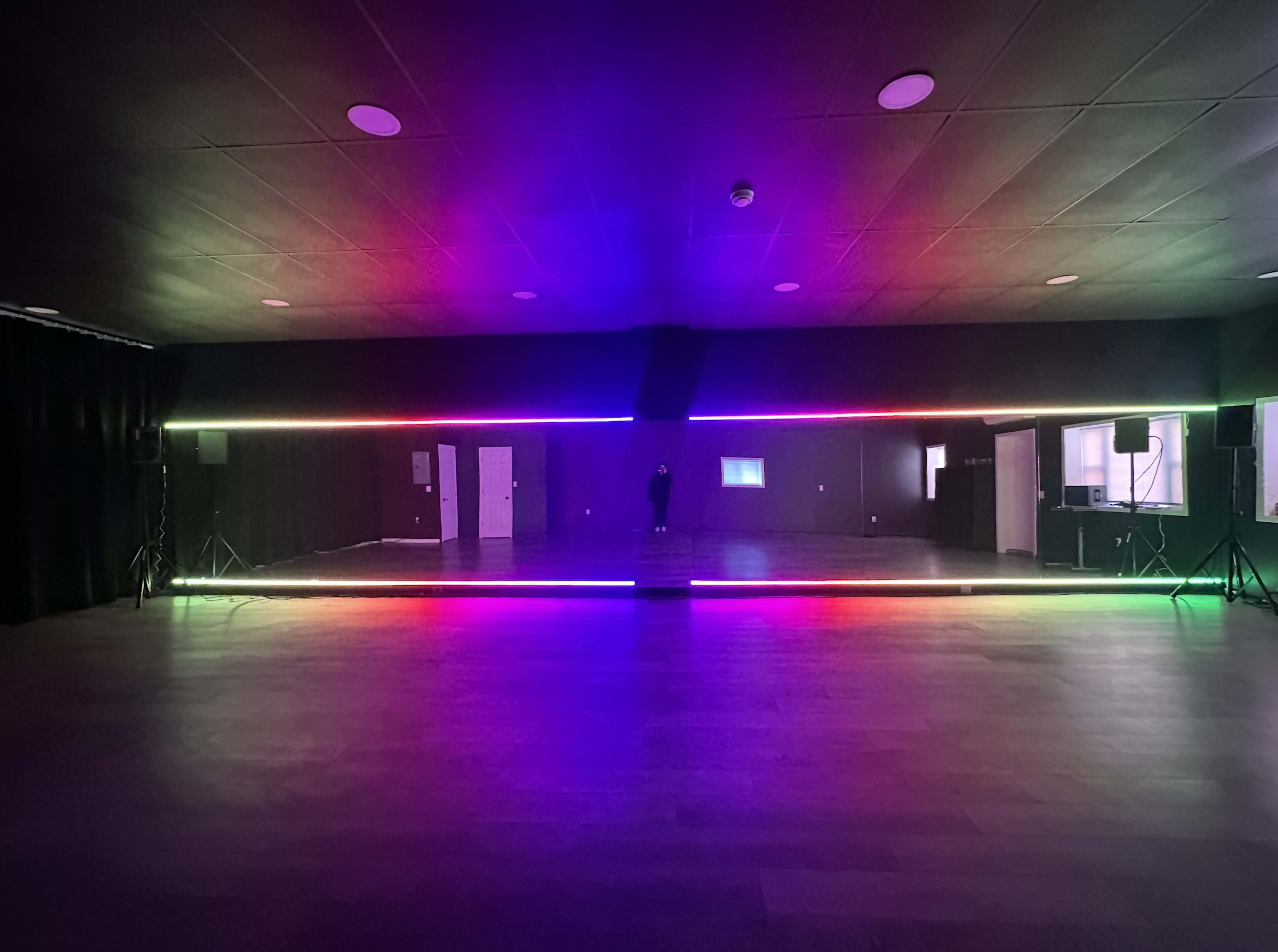 The image shows a large, dimly lit room with a brightly illuminated LED strip creating a colorful border along the floor.