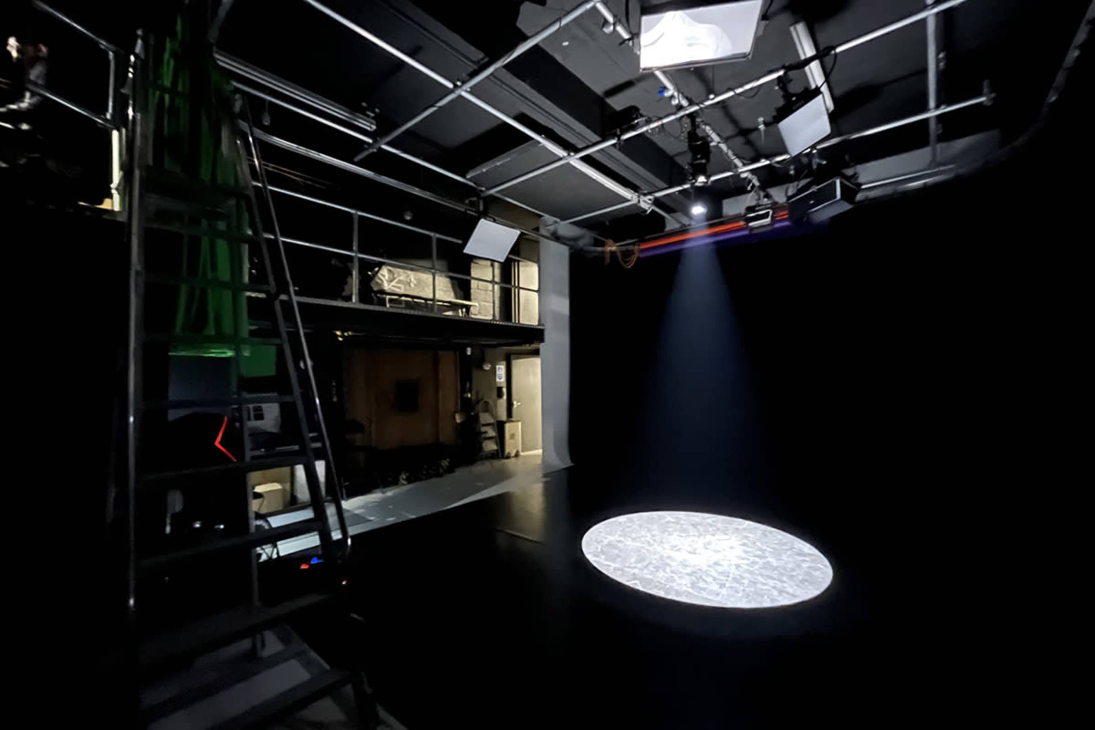 An empty stage with a circular spotlight illuminating the floor in a darkened studio.
