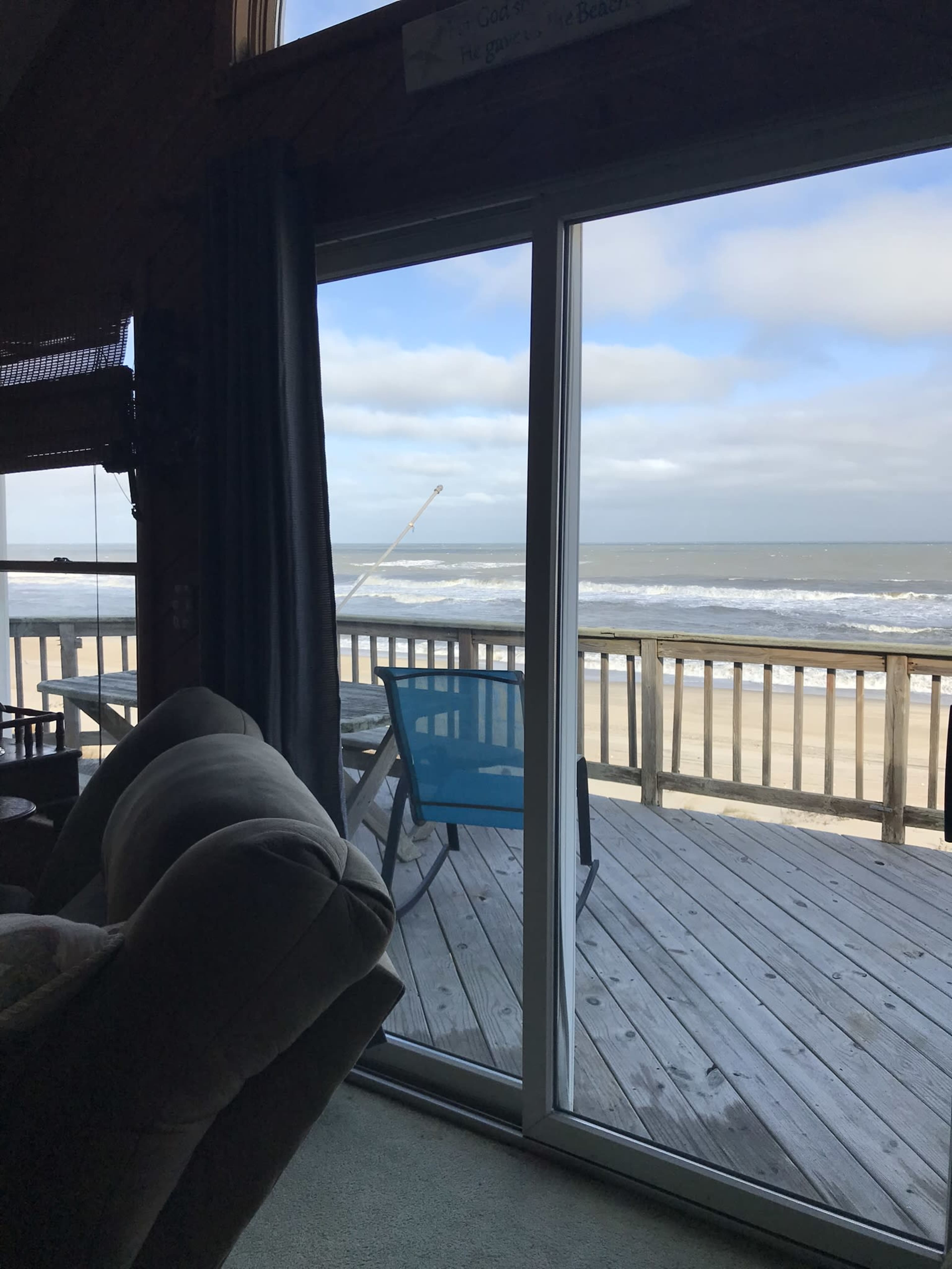 A large window frames a view of a beach with waves and a fishing pole set up on the deck.