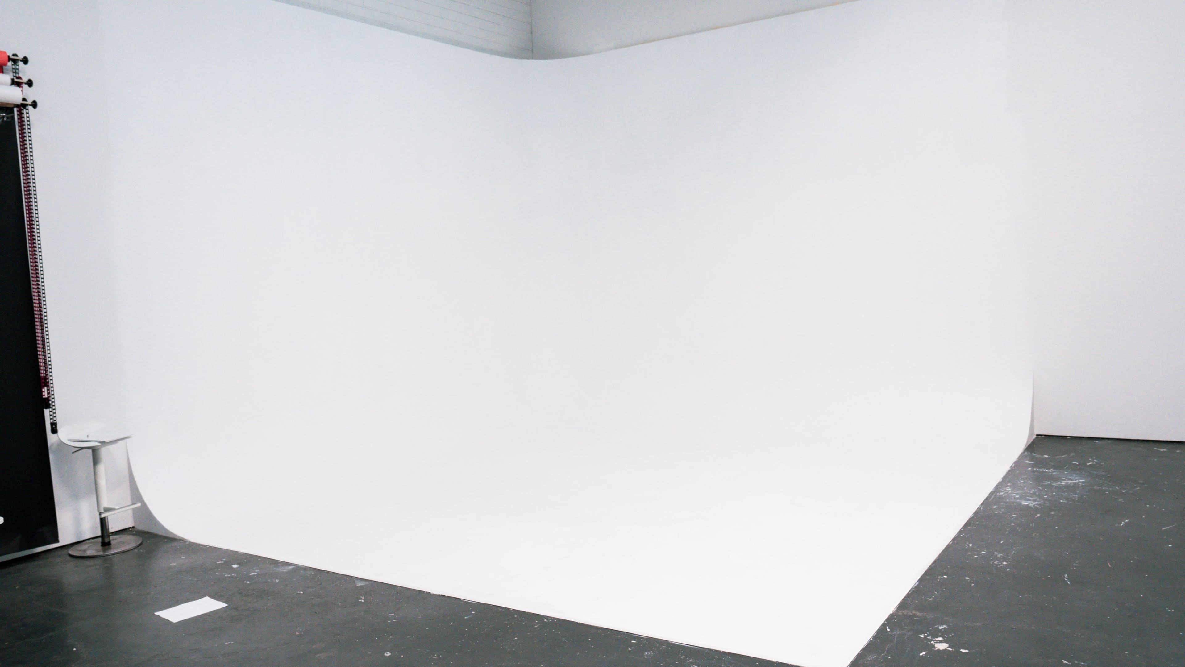 The image shows a photography studio with a seamless white backdrop and a gray floor.
