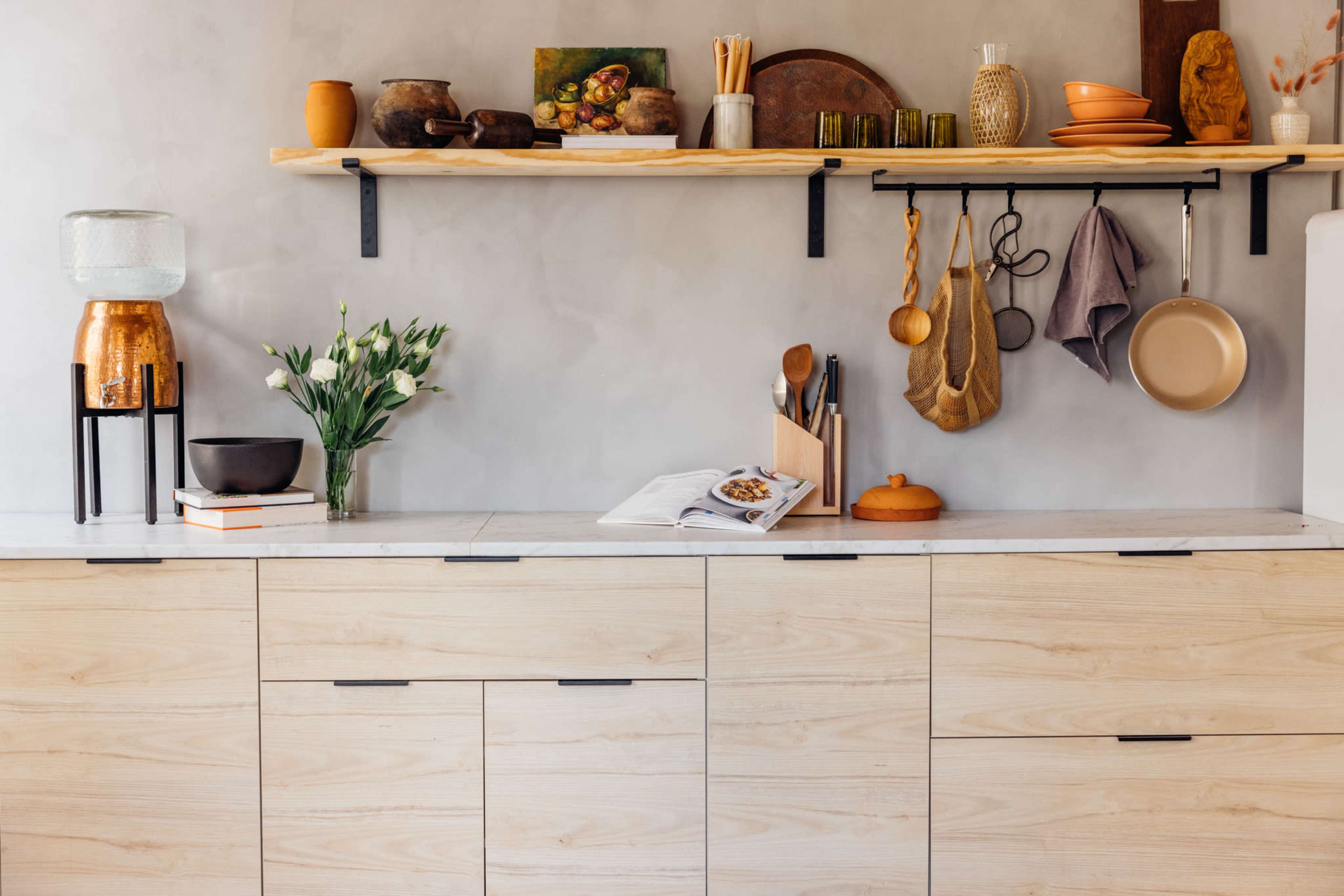 A modern kitchen features a minimalist wooden cabinet with open shelving displaying various kitchenware and a vase of flowers.