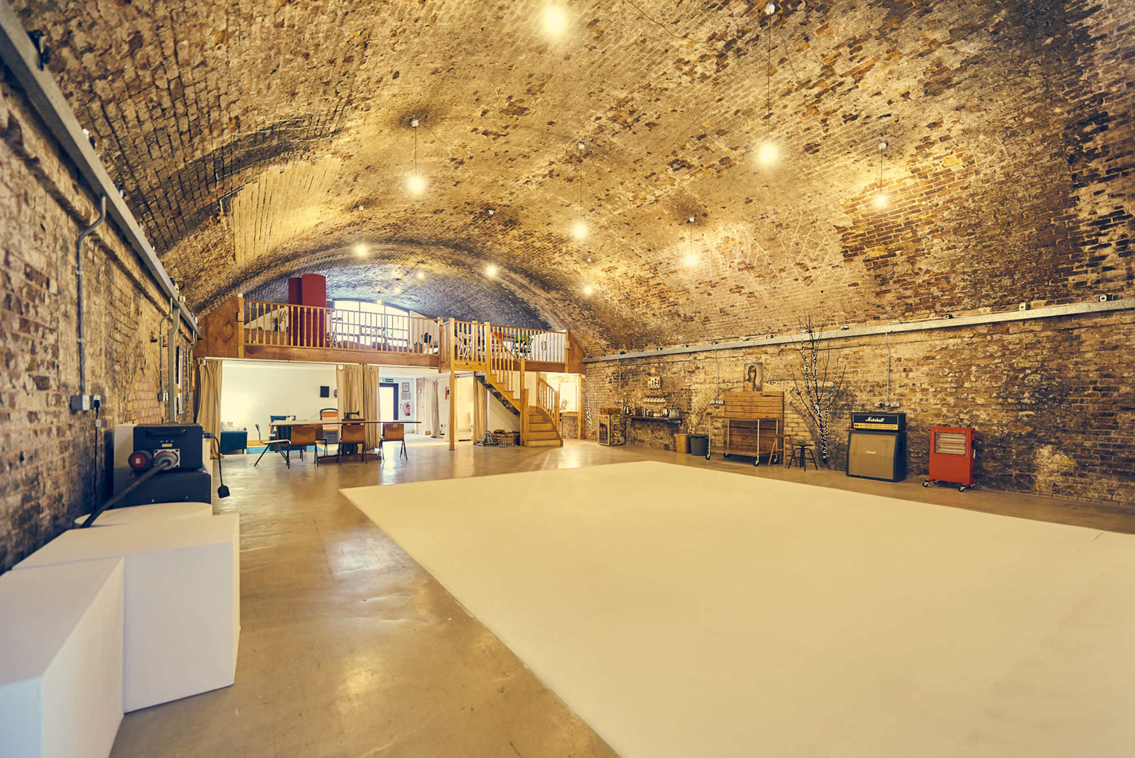 A spacious room with a high, arched brick ceiling, featuring a light-colored floor and various furnishings along the walls.