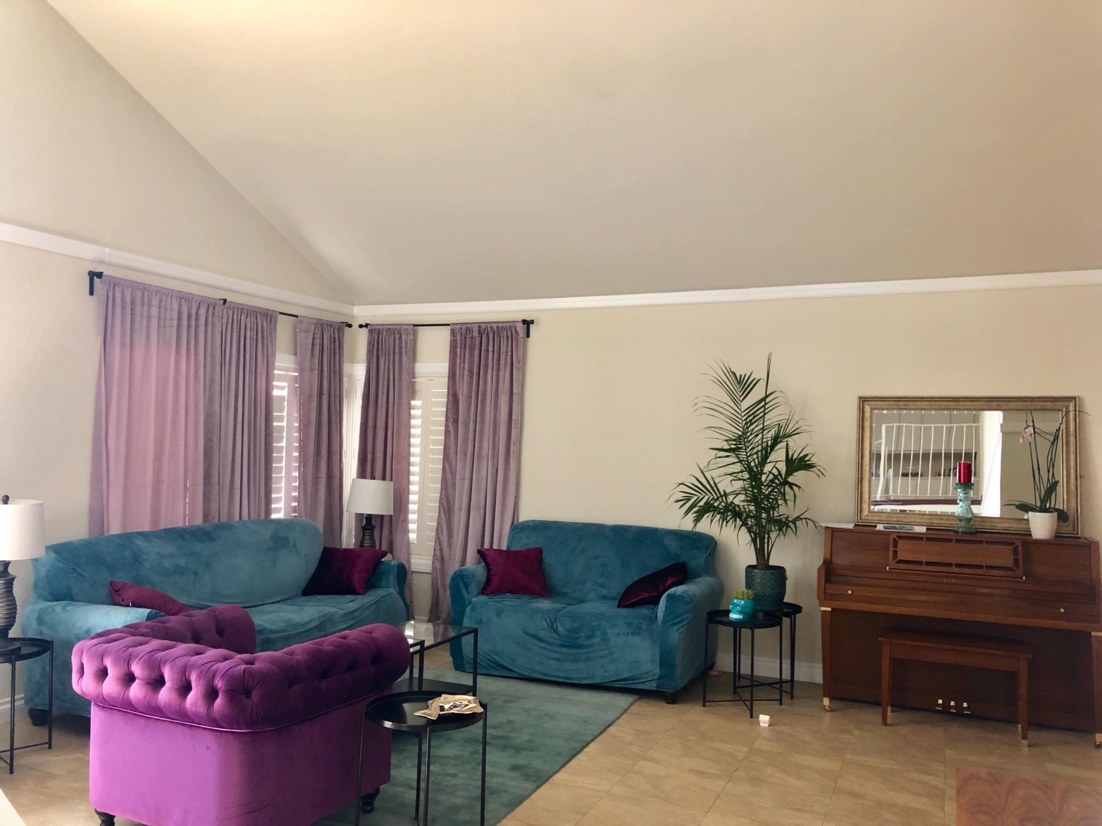 The living room features teal sofas, a purple tufted chair, and a wooden piano, surrounded by light curtains and a potted plant.