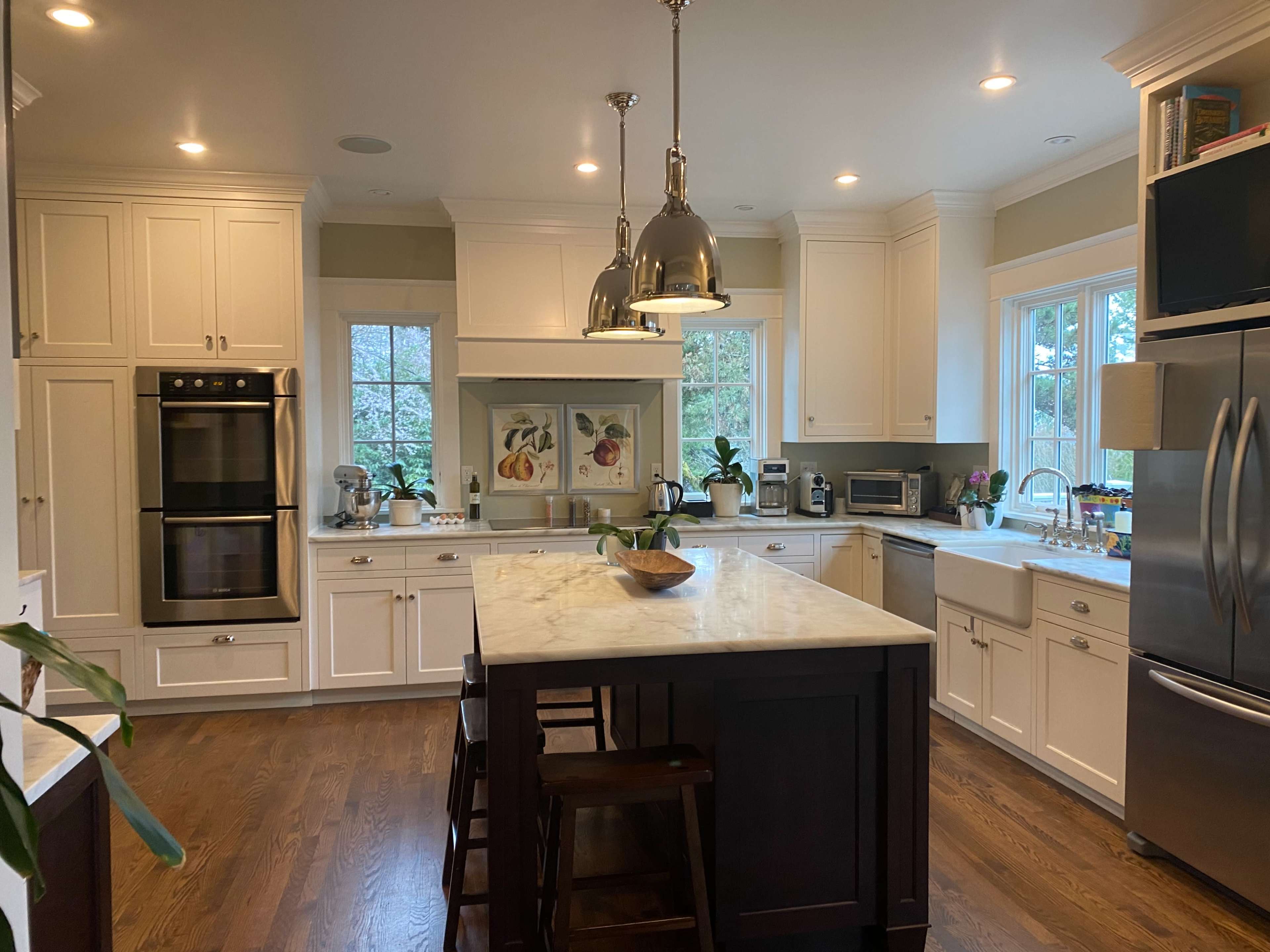 A brightly lit kitchen features white cabinetry, a central island with dark wood, and stainless steel appliances.