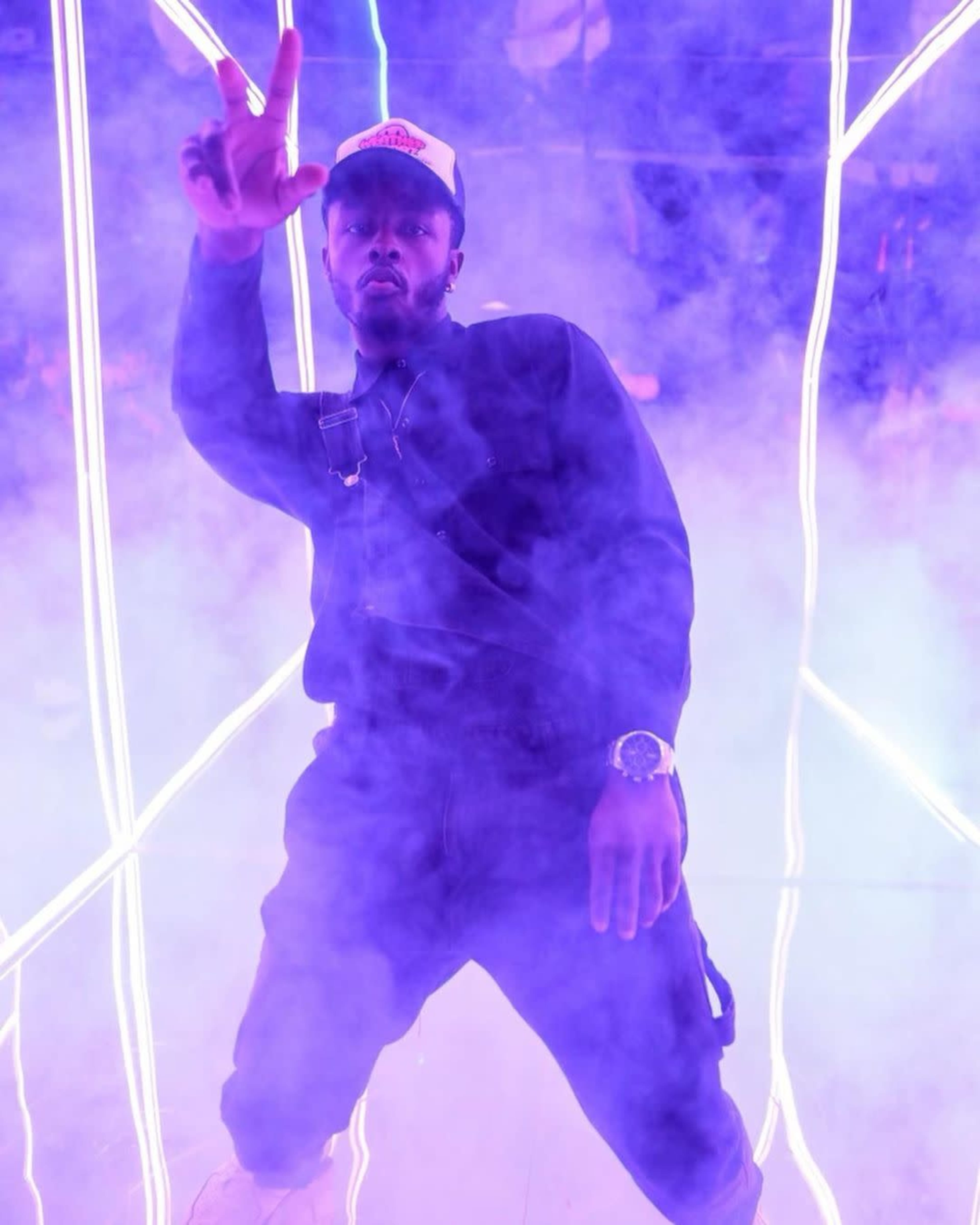 A person poses with a peace sign in a fog-filled space illuminated by neon lights.