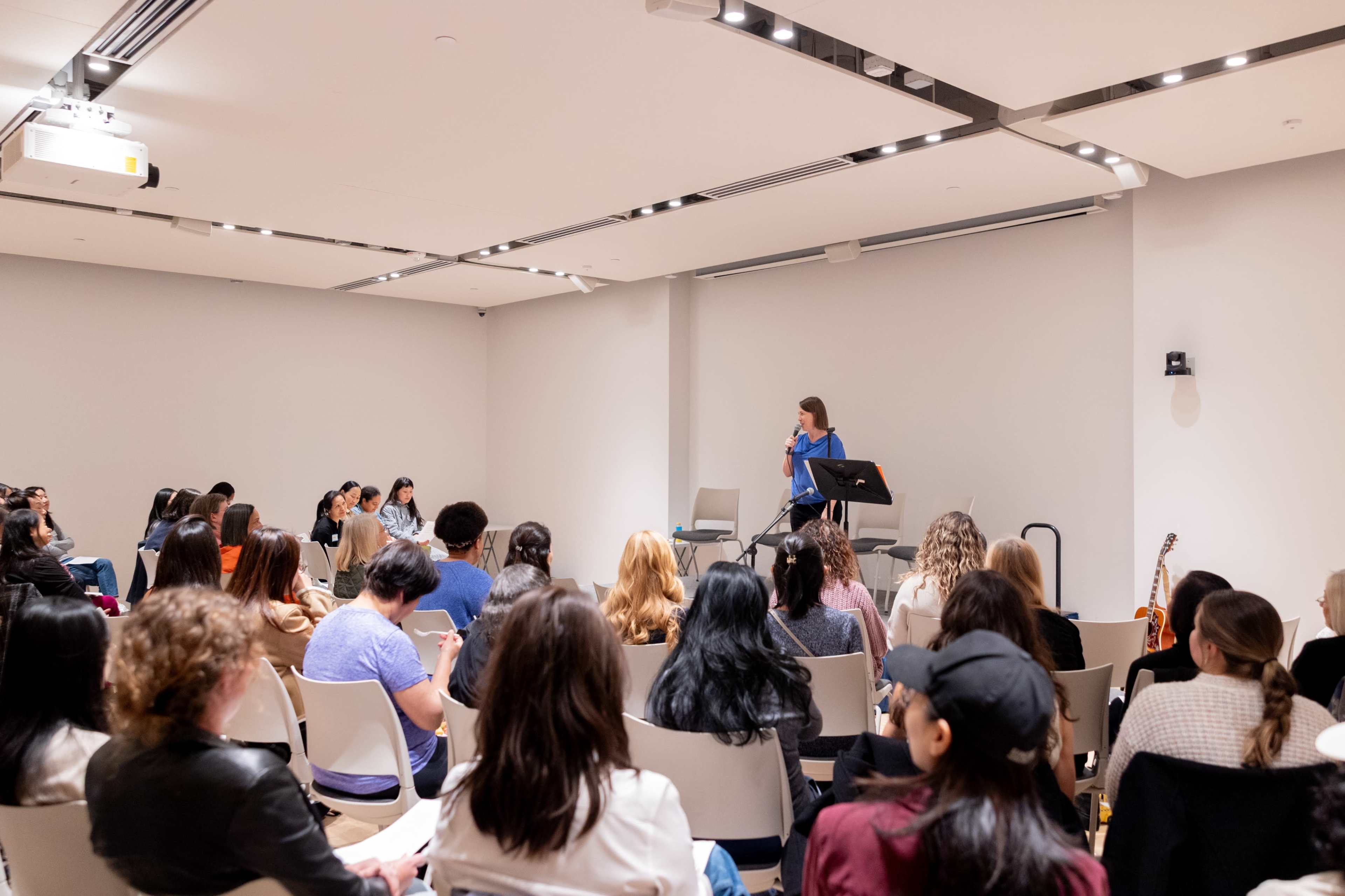 A speaker stands at a podium in front of an audience seated in a conference room.