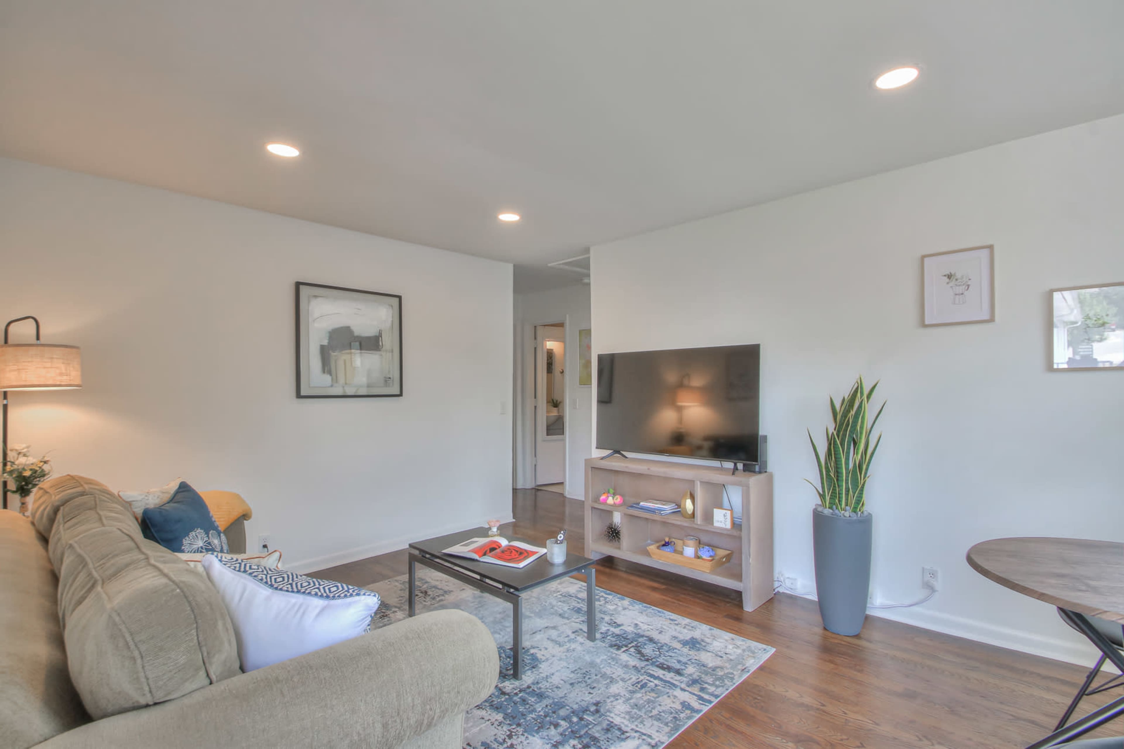 A modern living room features a beige sofa, a coffee table with decorative items, and a television on a light wooden stand, surrounded by minimalist decor.