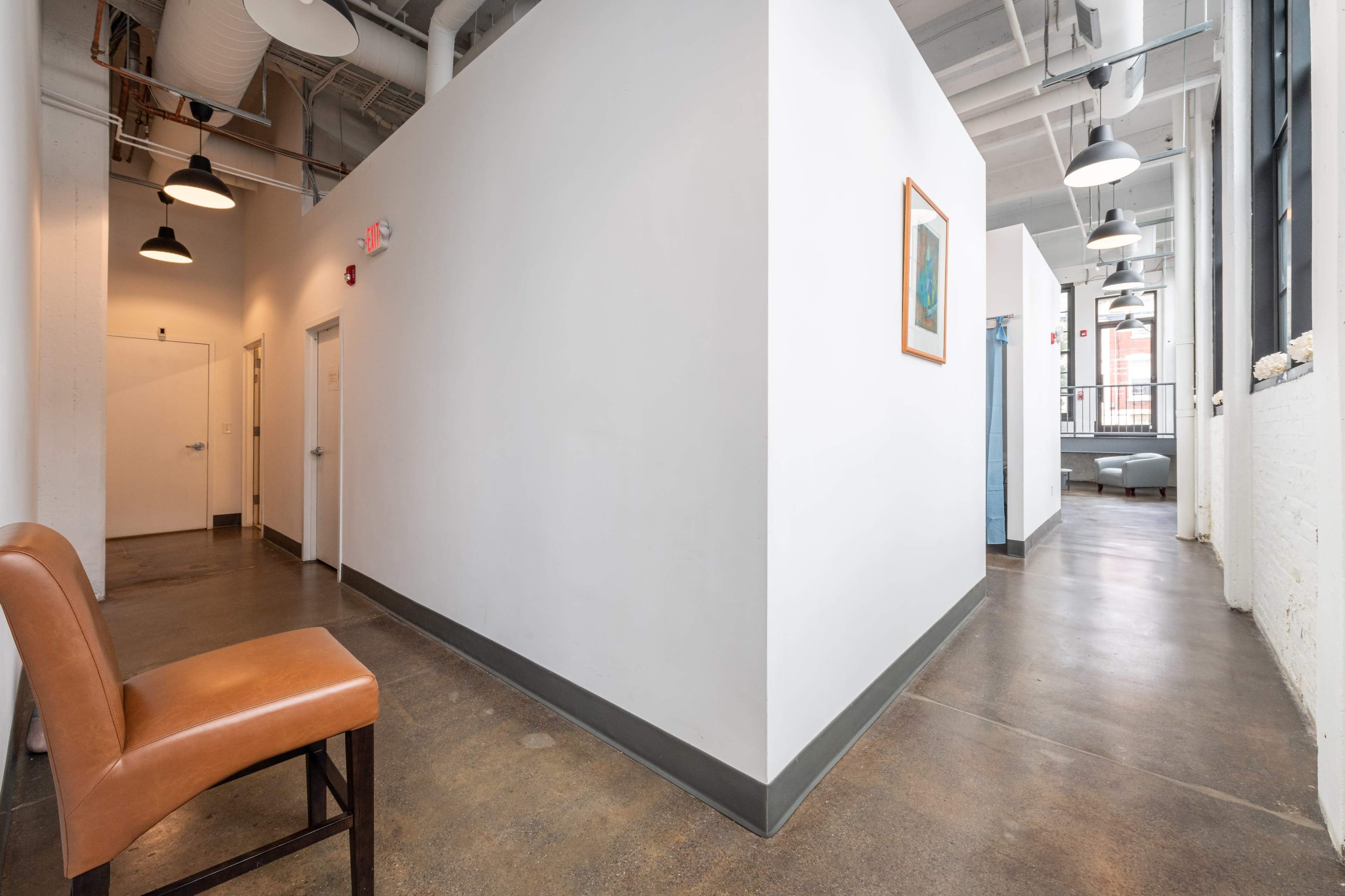 A clear hallway with a brown chair and doors on either side leads to a blue wall at the end.