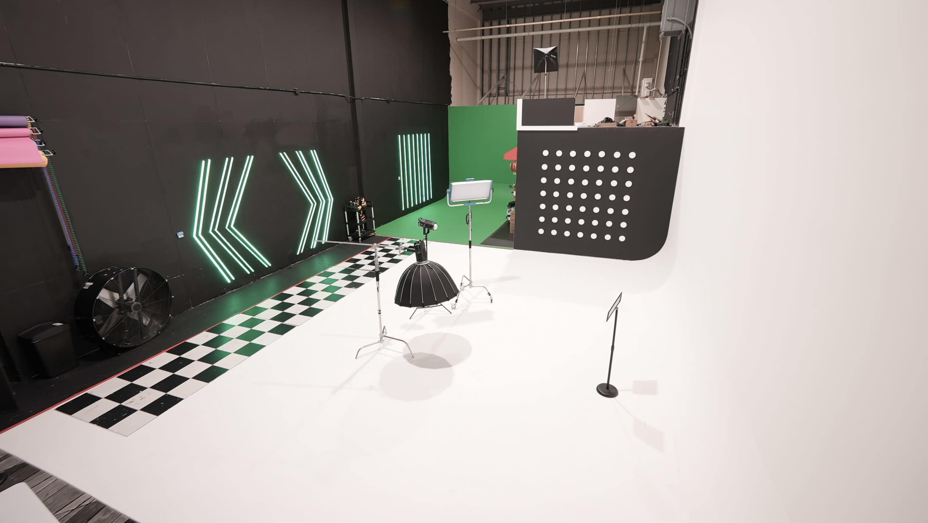 The image shows a photography studio with a checkered floor, a white backdrop, and various lighting equipment set up alongside geometric wall designs.