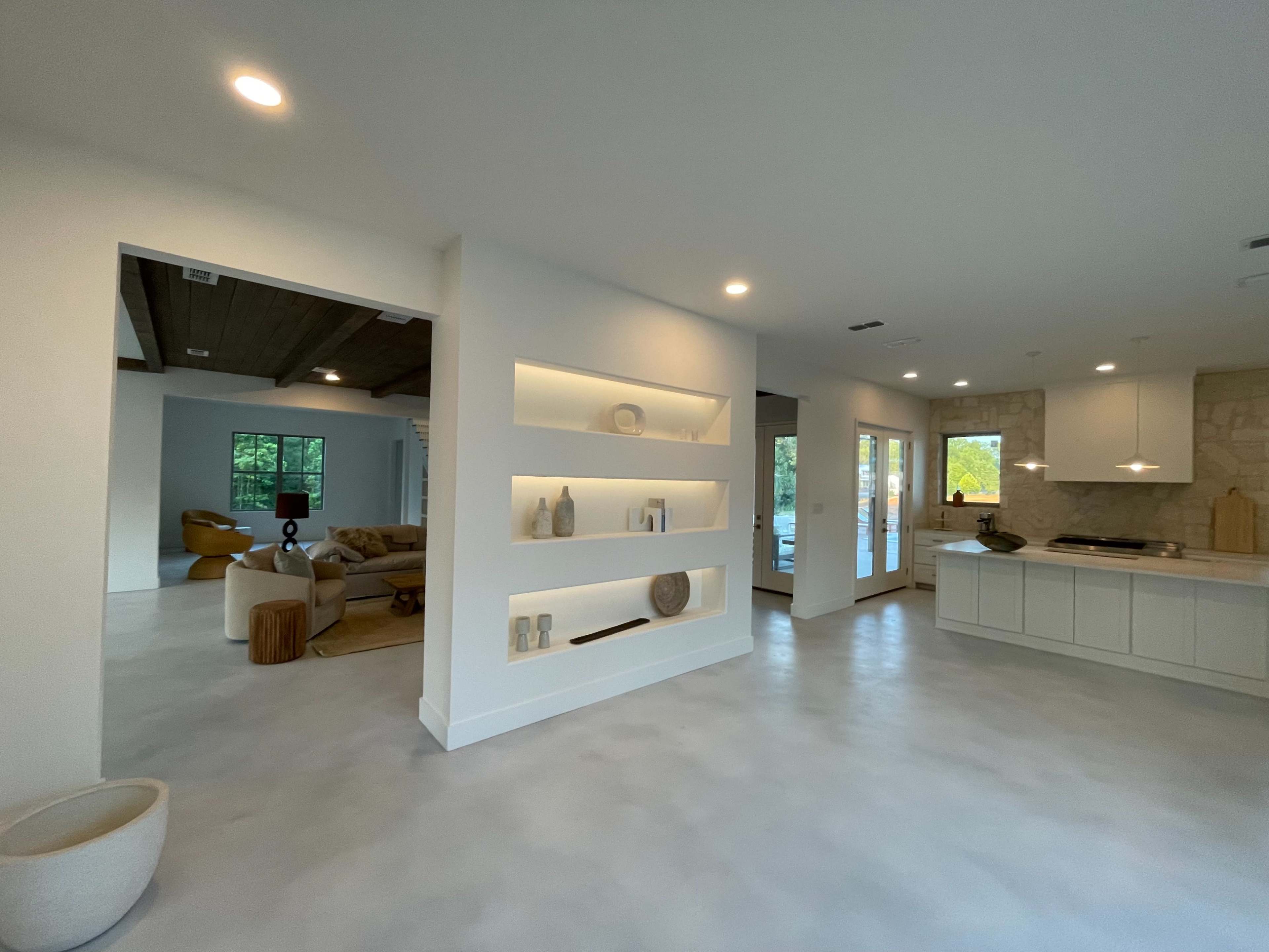 A bright, modern living space features a minimalist shelf display and an open layout connecting to a cozy lounge area.