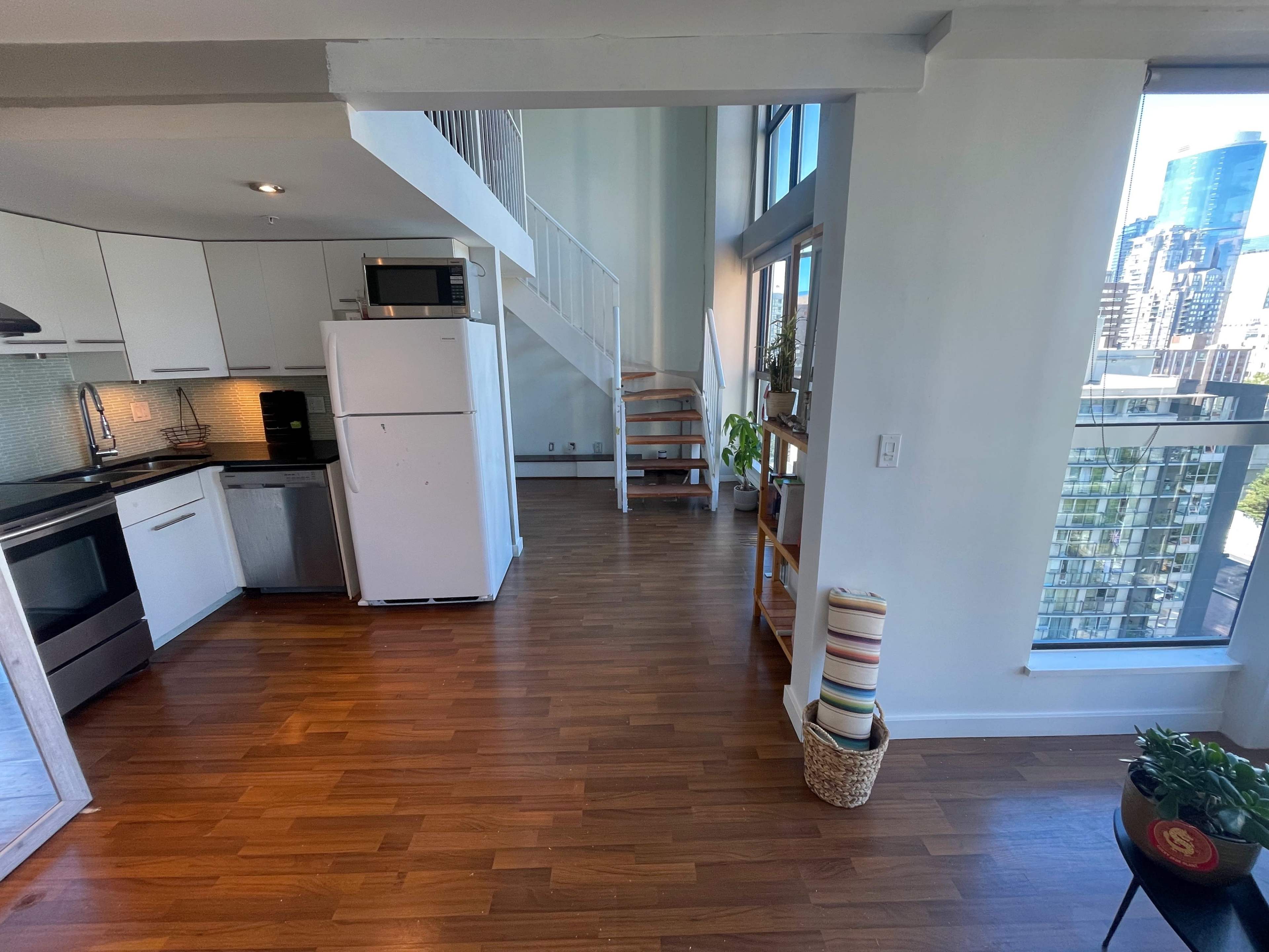 A modern open-concept apartment with a kitchen area, a white refrigerator, and a spiral staircase leading to an upper level.